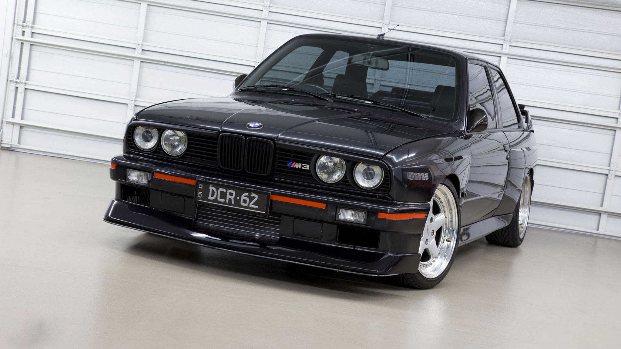 classic bmw 桌布 壁紙 — 一輛時尚的黑色BMW M3跑車帶有橙色點綴，停在潔白的車庫中。