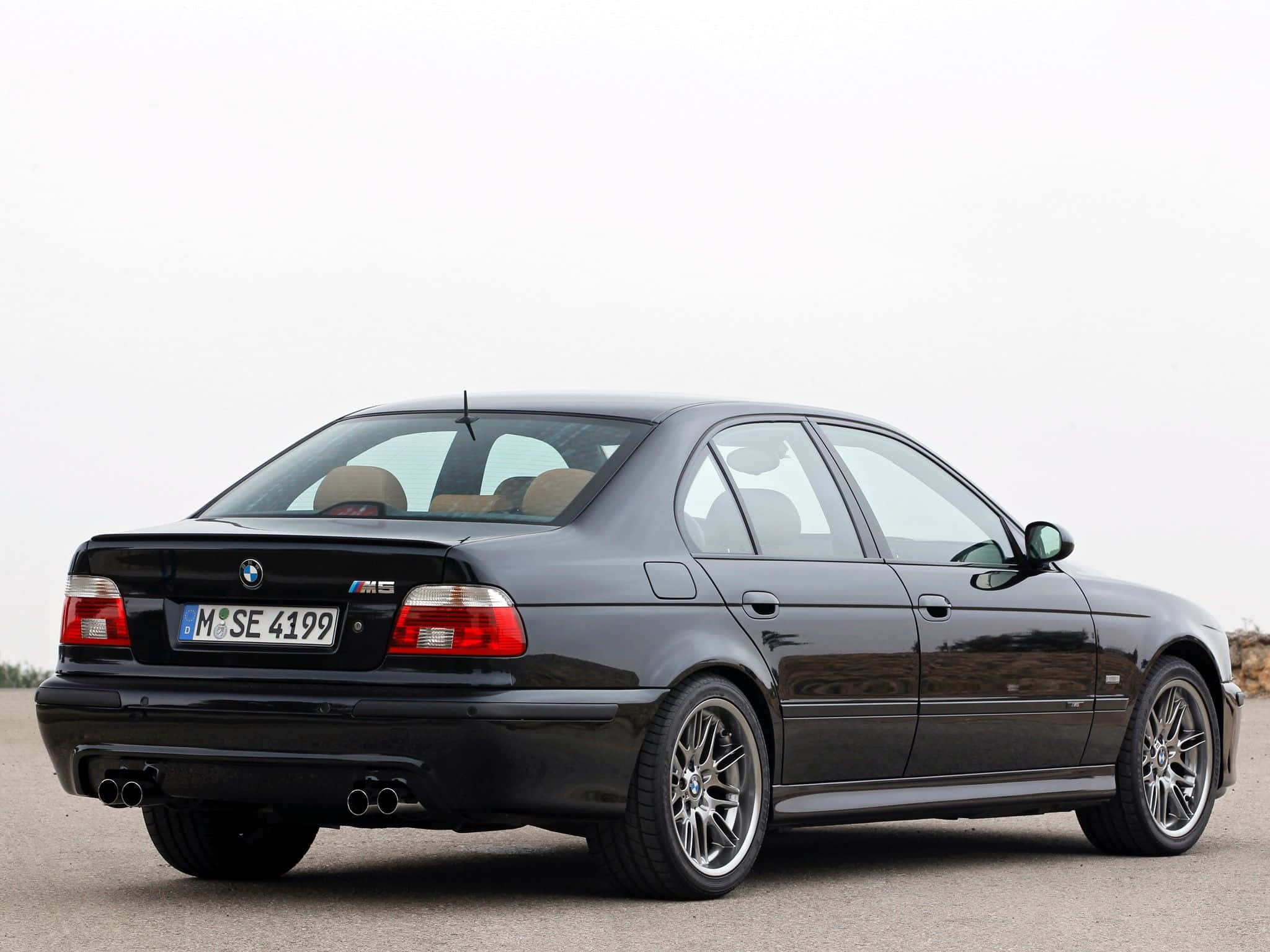 Bmw M5 桌布 壁紙 — 一輛時尚的黑色BMW M5轎車停在瀝青路上，背景是簡約的多雲天空。