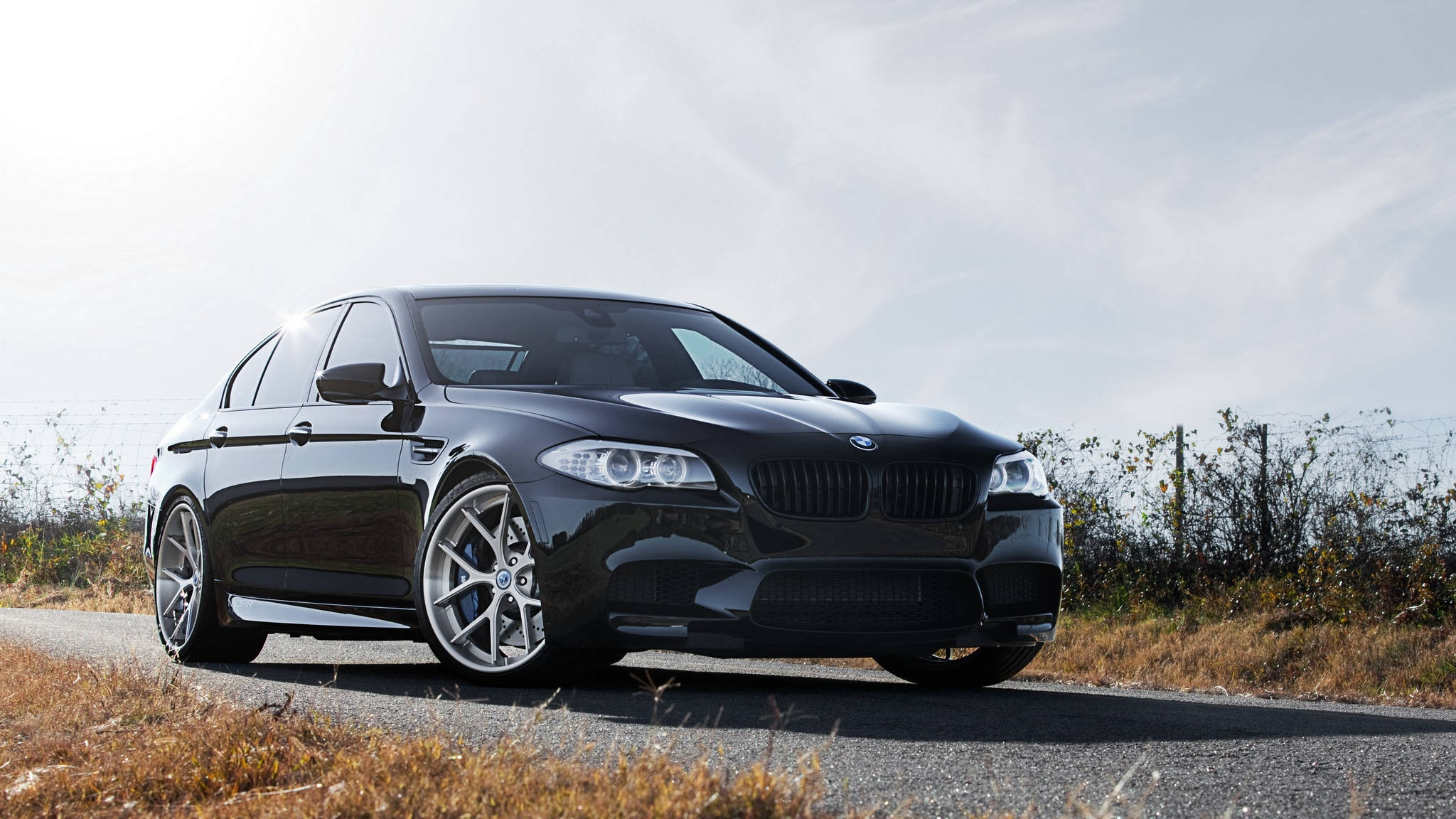 黑色 桌布 壁紙 — 一輛時尚的黑色BMW M5運動轎車停在乾草和陰天的鄉村道路上。