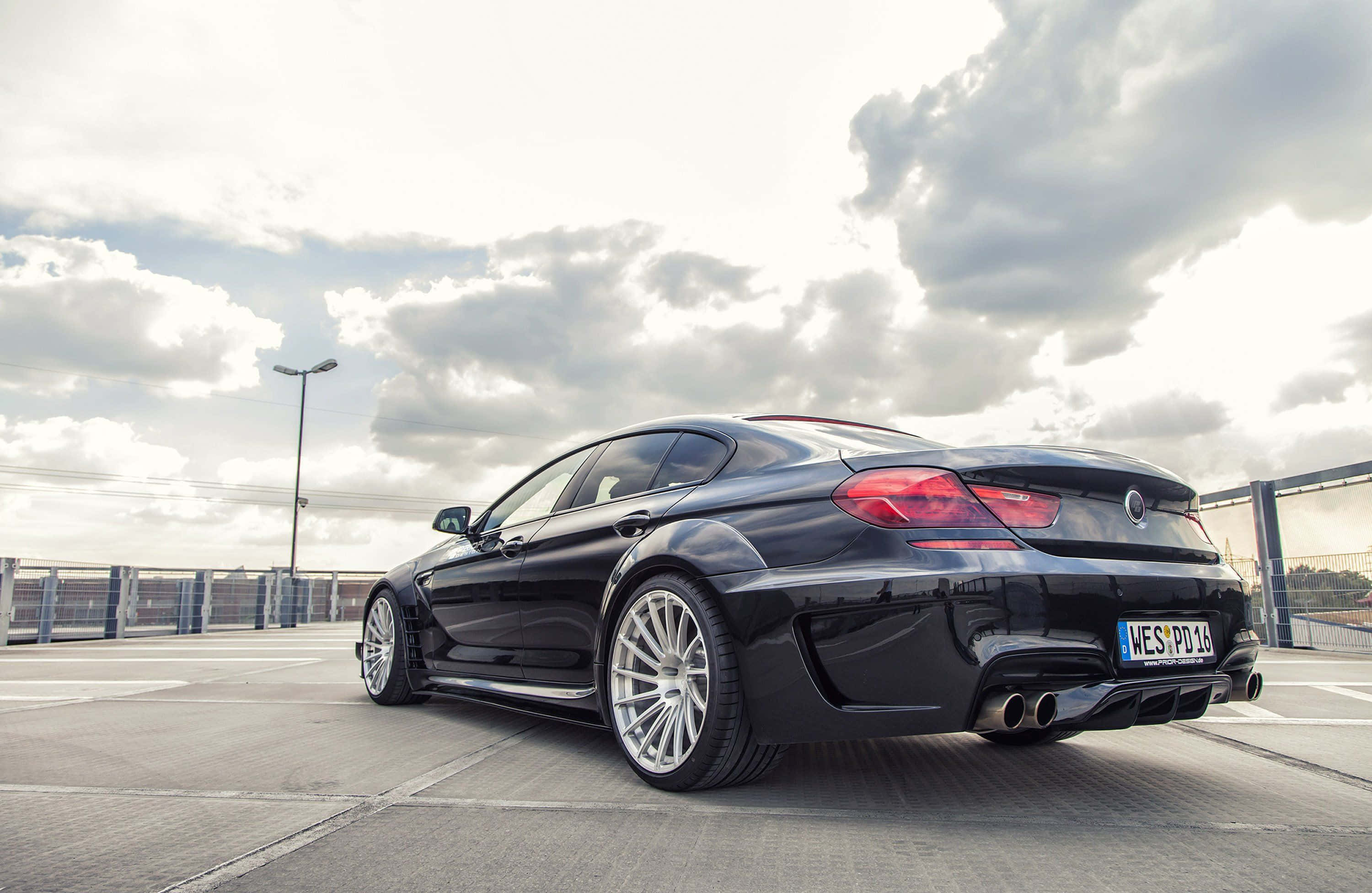 Bmw 6 Series 桌布 壁紙 — 一輛時尚的黑色BMW M6跑車停泊在陰天，天空戲劇性，銀色輪圈反射光線。