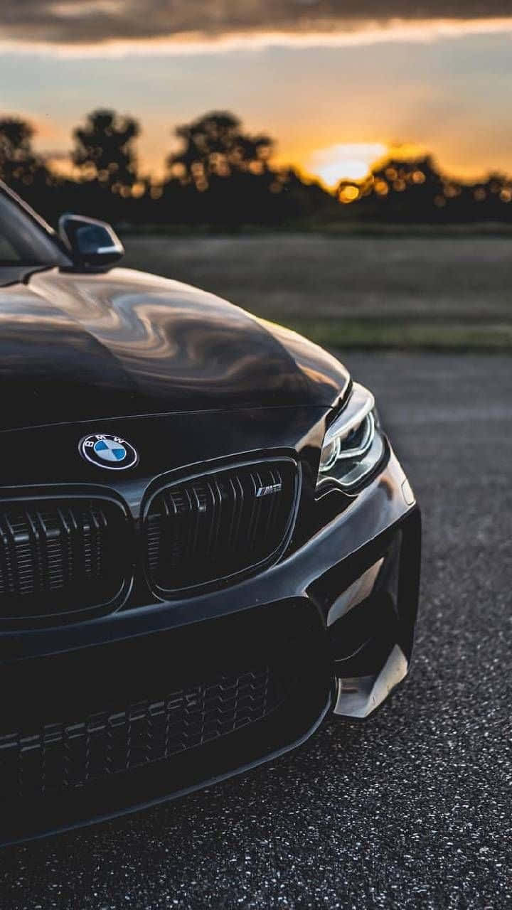 BMW 動圖 桌布 壁紙 — 一輛時尚的黑色BMW M汽車在金色日落光線下閃耀，行駛在瀝青路上，背景是模糊的樹木。