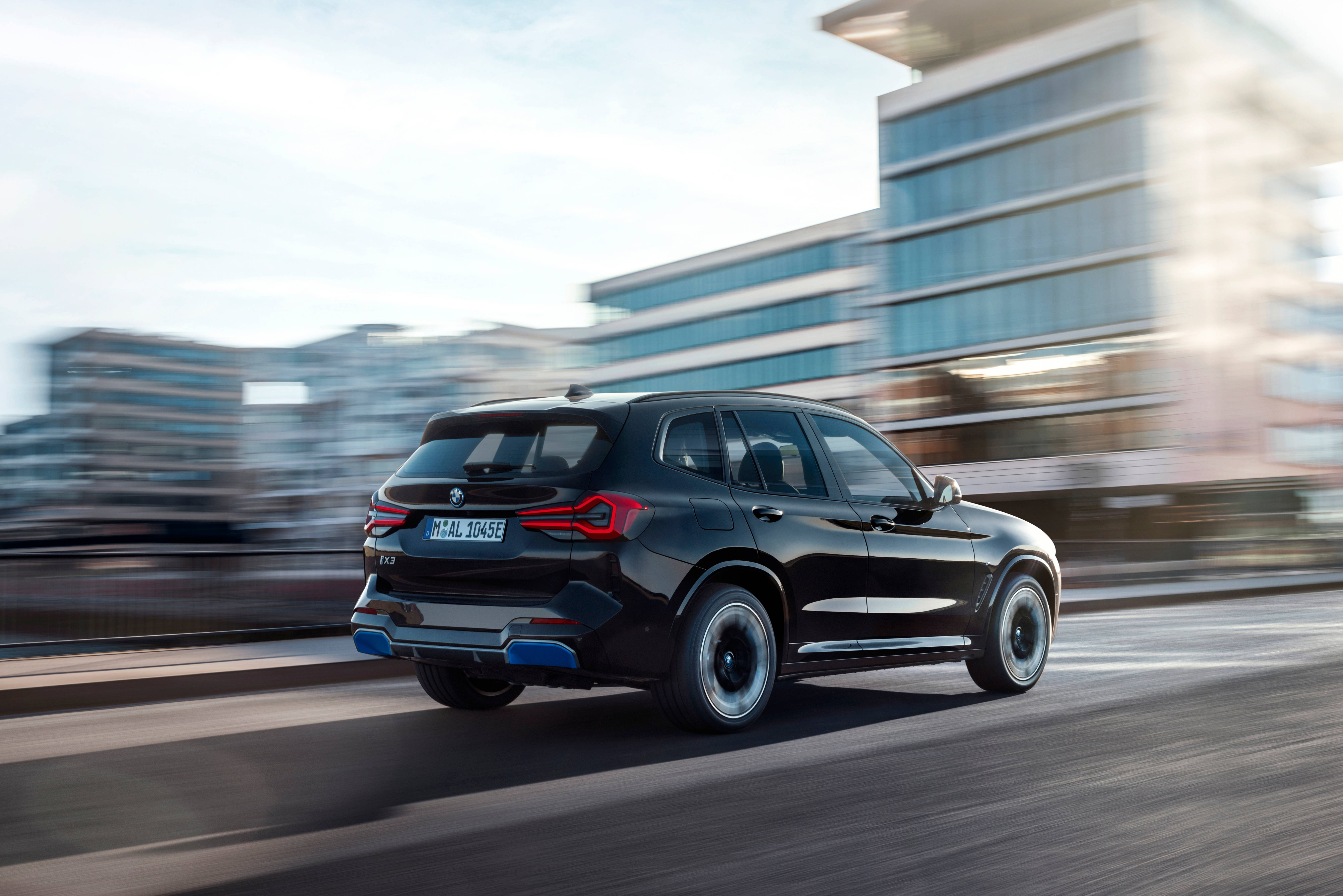 Black Bmw 桌布 壁紙 — 一輛時尚的黑色BMW SUV在現代城市景觀中疾馳，背景帶有動態模糊效果。