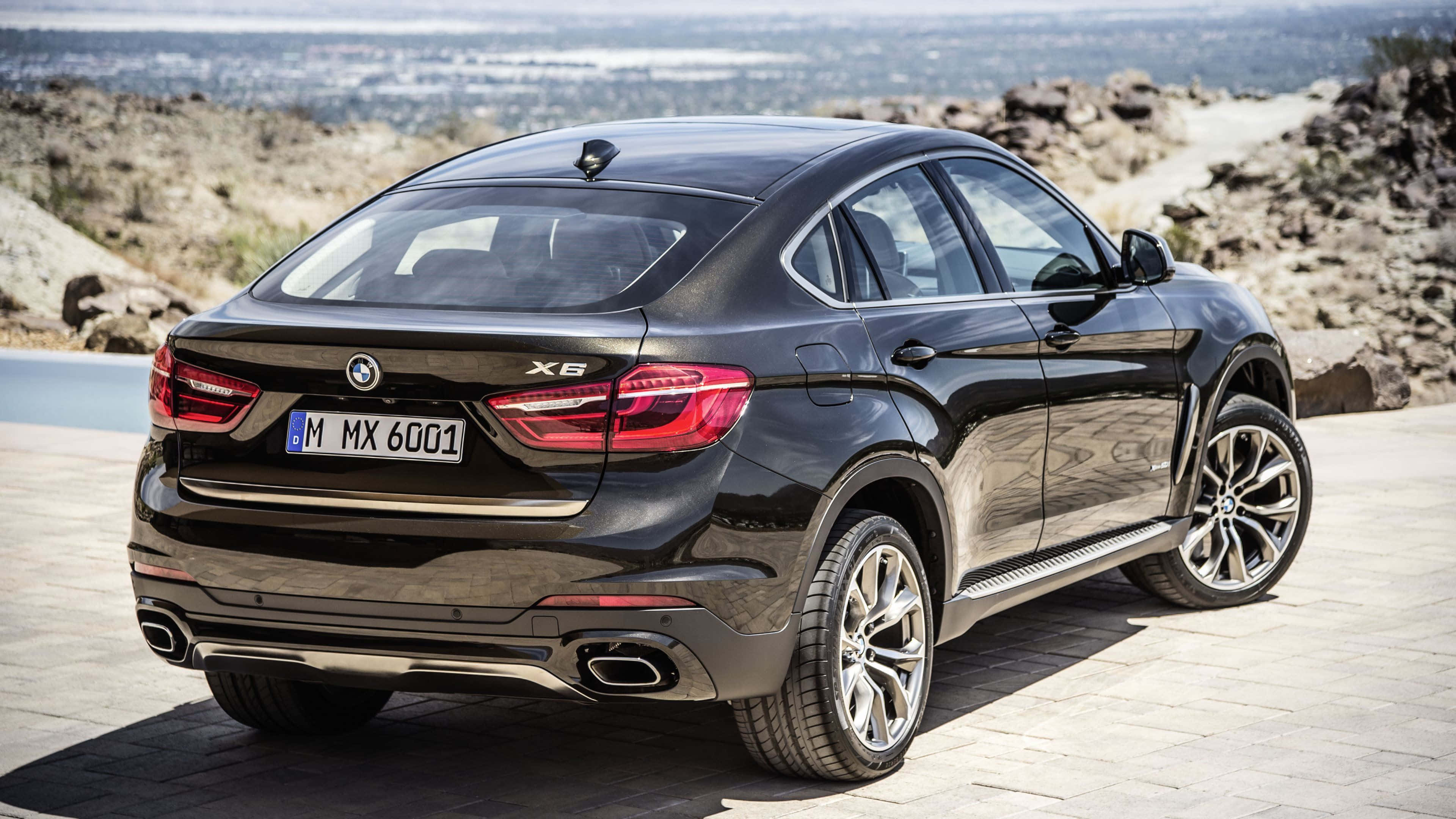 Bmw X6 桌布 壁紙 — 一輛時尚的黑色BMW X6 SUV停泊在石頭觀景台上，遠方城市景觀在明亮日光下清晰可見。