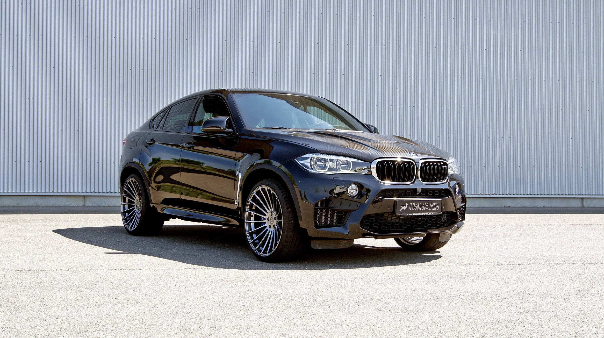 m 桌布 壁紙 — 一輛時尚的黑色BMW X6M運動轎跑車停在混凝土上，背景是波紋金屬牆，在明亮的日光下。