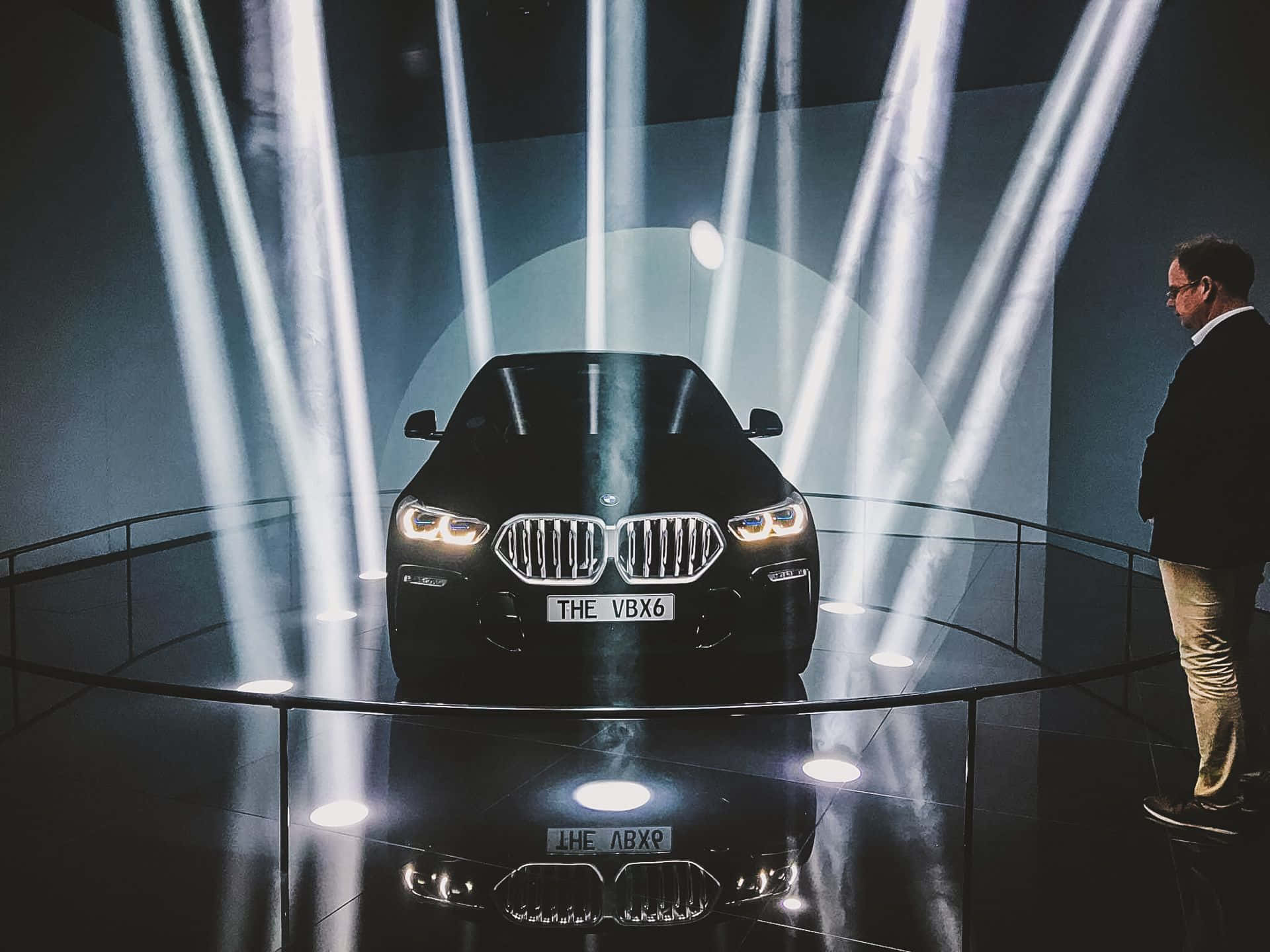 Vantablack 桌布 壁紙 — 一輛時尚的黑色BMW X6在反射舞台上被垂直聚光燈戲劇性地照亮，一名男子從側面觀察。
