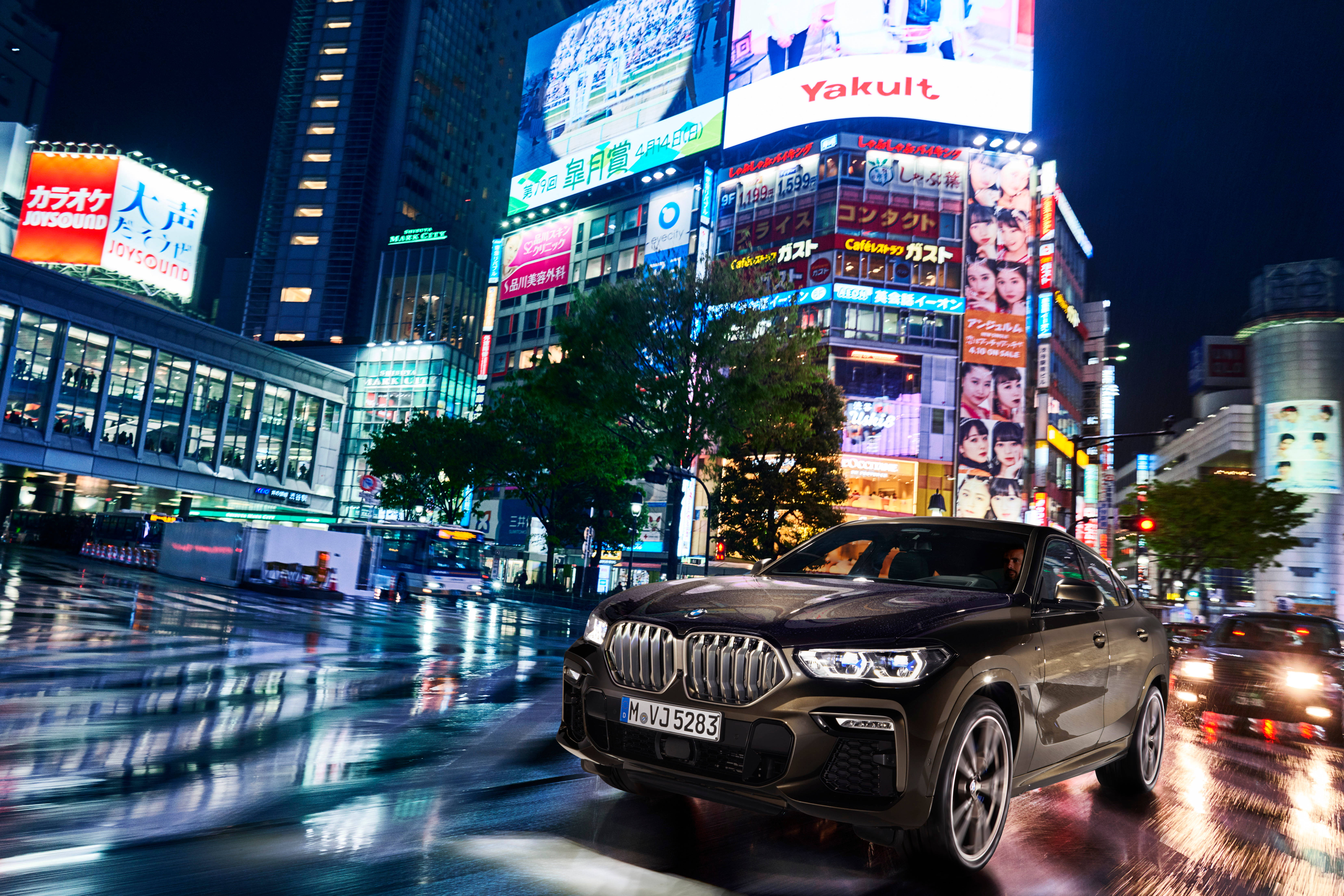 m 桌布 壁紙 — 一輛時尚的黑色BMW X6在雨濕的東京夜街上飛馳，四周是耀眼的霓虹燈招牌和發光的摩天大樓。