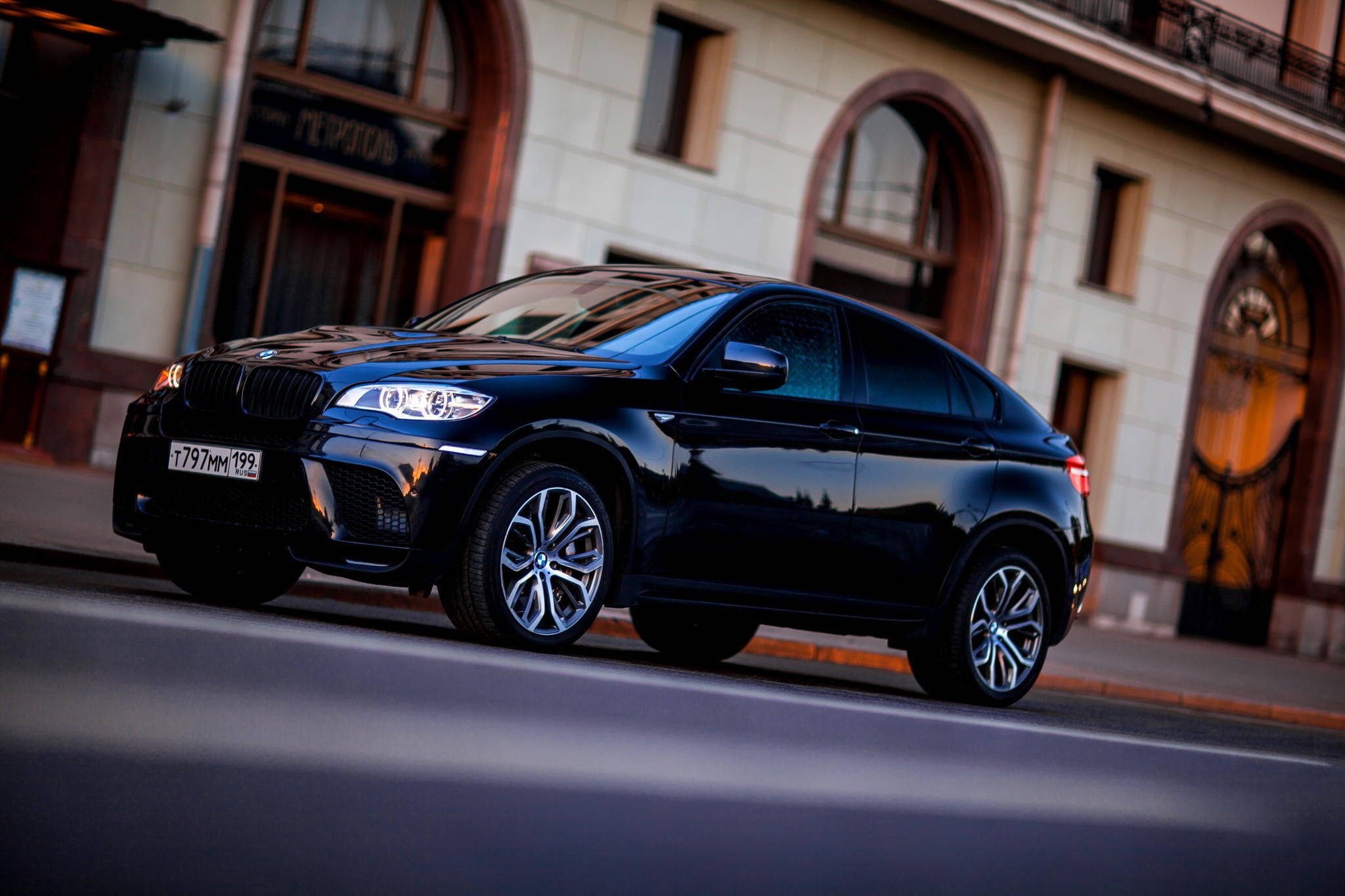 m 桌布 壁紙 — 一輛時尚的黑色BMW X6運動型轎跑車在黃昏時分沿著城市街道滑行，溫暖的建築燈光反射在其光滑的表面上。