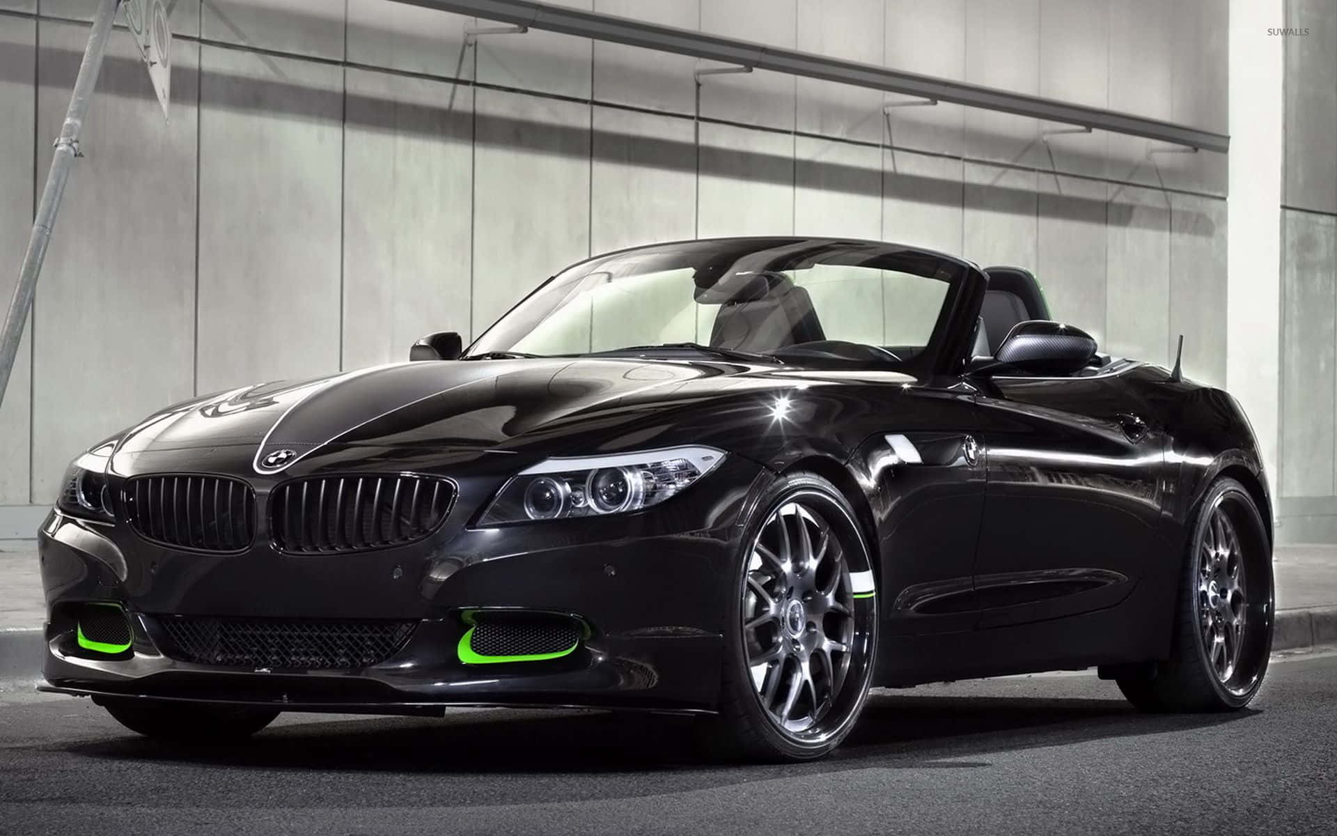 Bmw Z4 桌布 壁紙 — 一輛時尚的黑色BMW Z4敞篷車帶有螢光綠色點綴，在現代混凝土車庫的攝影棚燈光下閃閃發光。