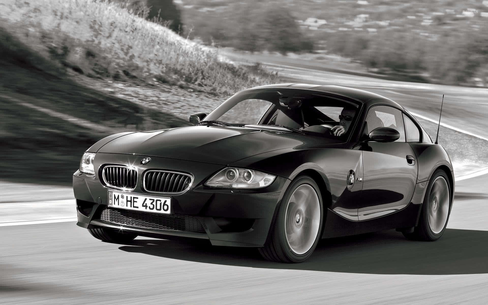 Bmw Z4 桌布 壁紙 — 一輛時尚的黑色BMW Z4跑車在蜿蜒的道路上行駛，帶有模糊的動感和丘陵背景。