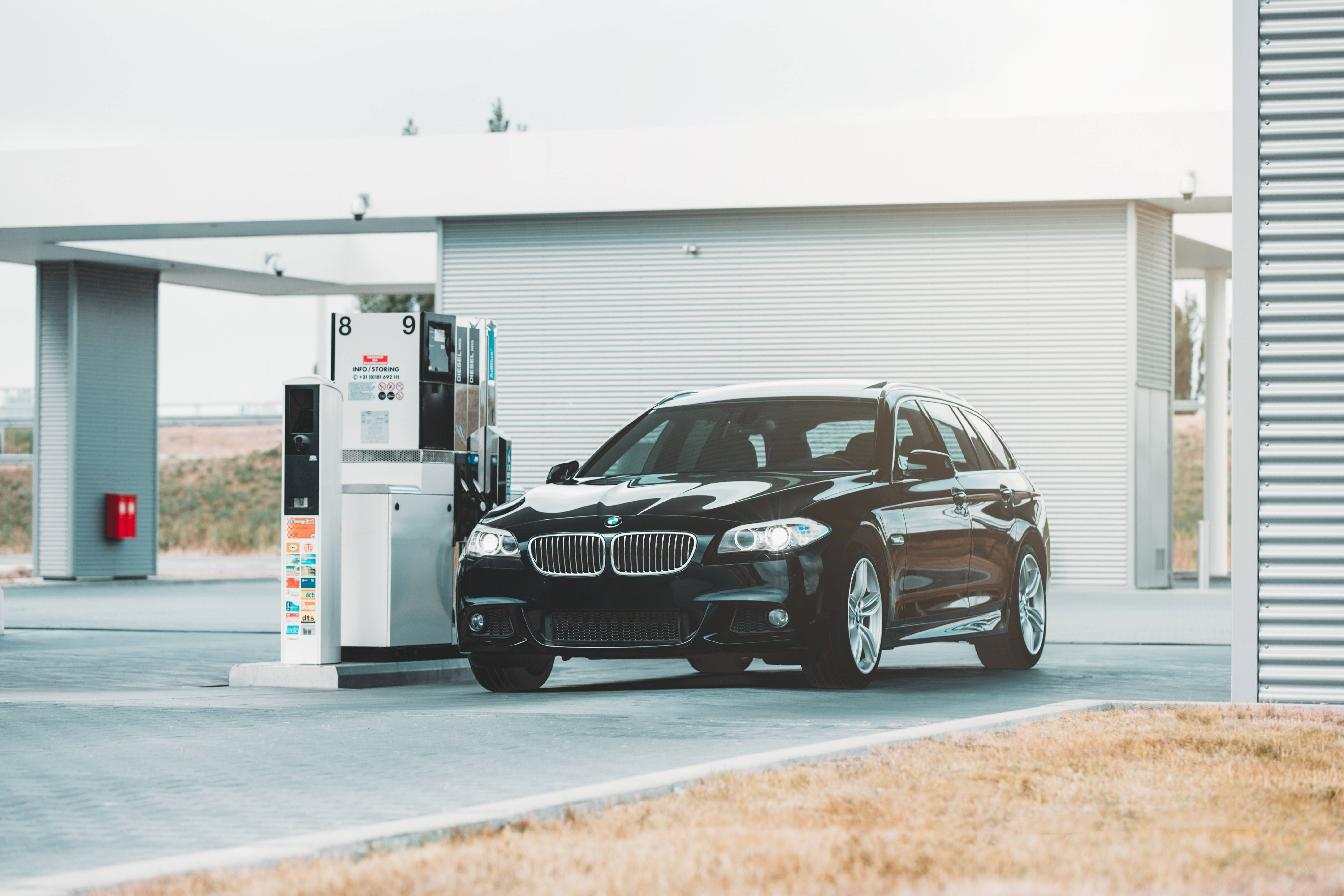 BMW 動圖 桌布 壁紙 — 一輛時尚的黑色BMW旅行車停放在現代化的加油站，天空多雲。