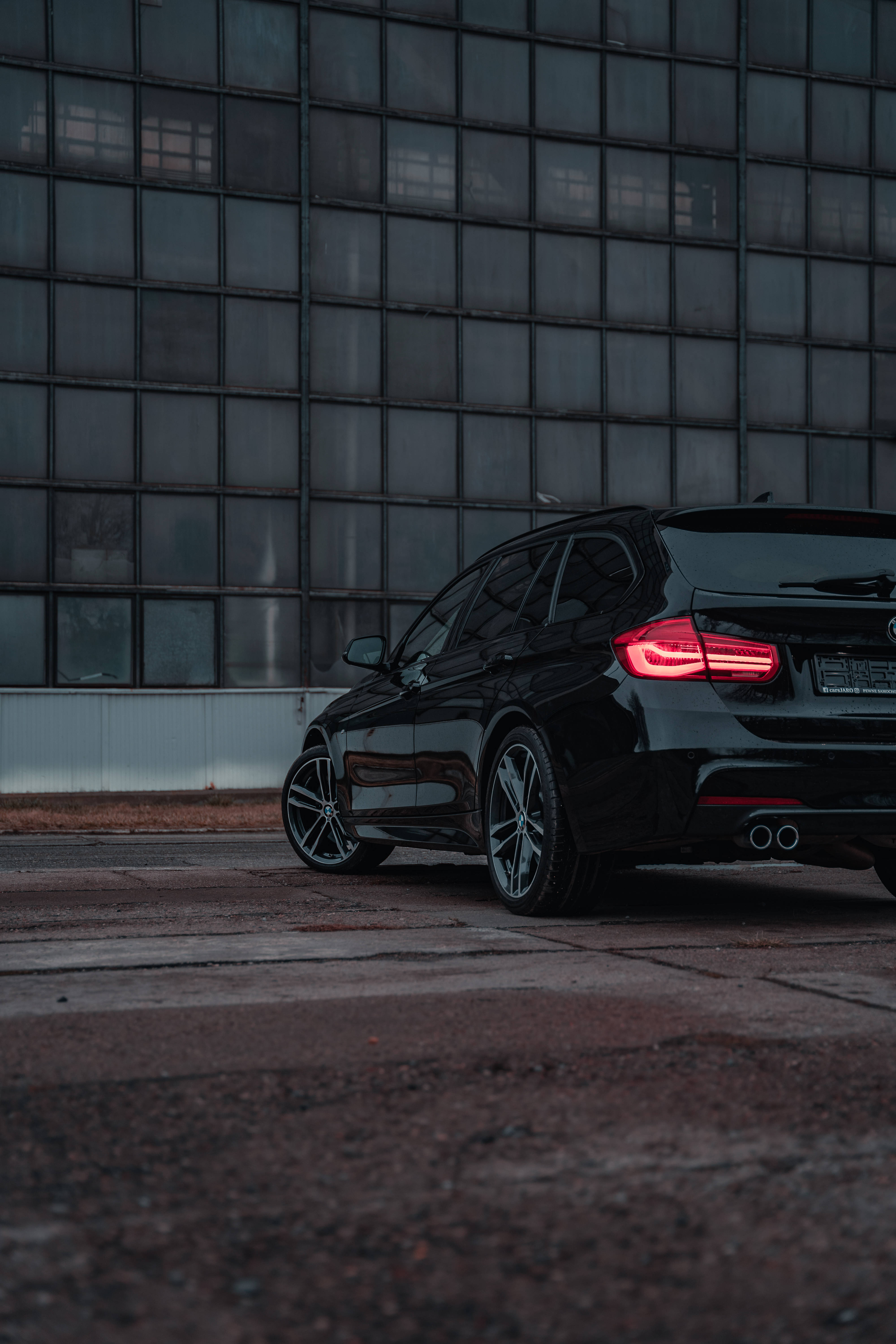 m 桌布 壁紙 — 一輛時尚的黑色BMW旅行車在黃昏時停靠在網格狀玻璃建築前，紅色尾燈閃爍發光。