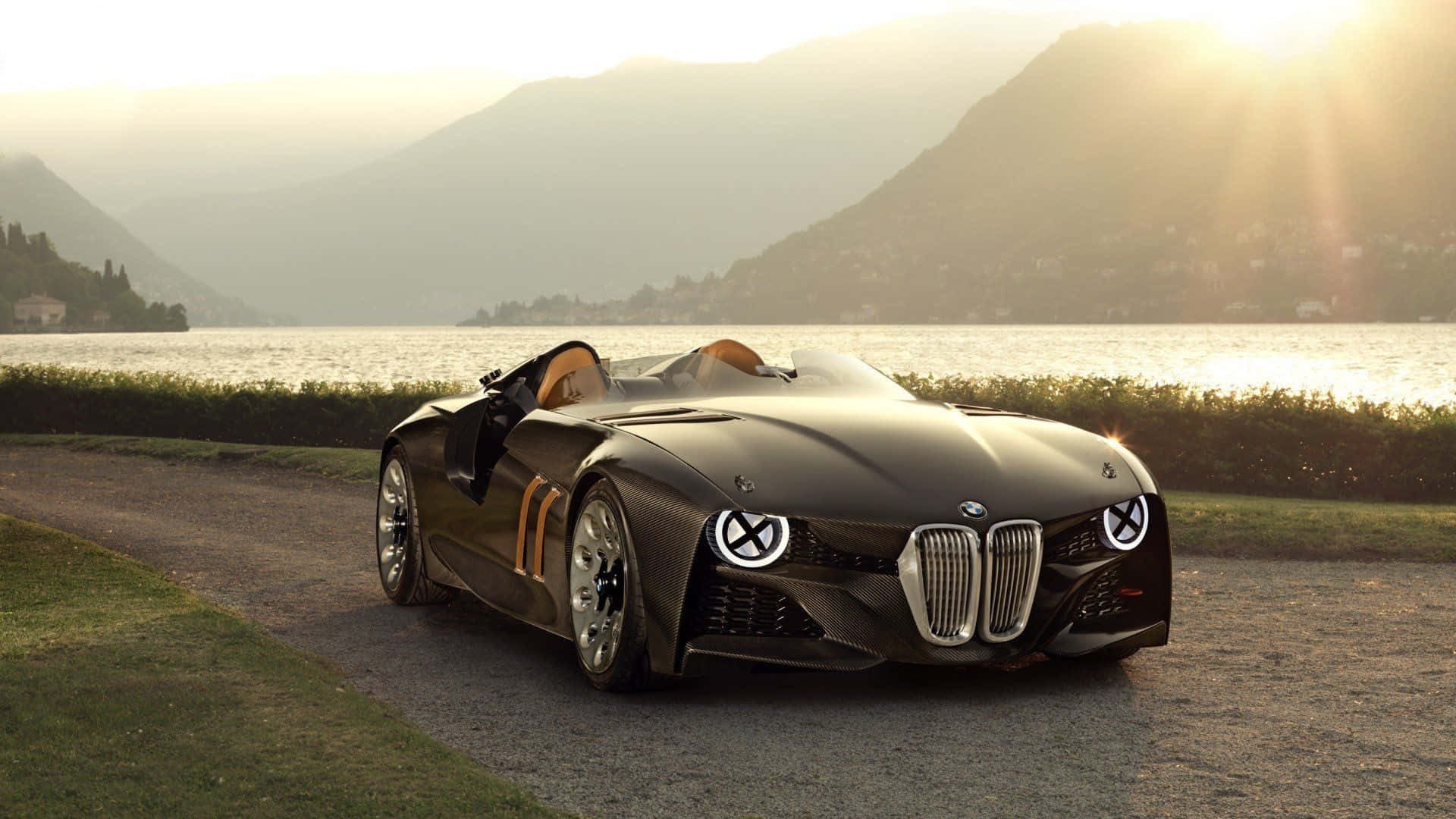 BMW 動圖 桌布 壁紙 — 一輛時尚的黑色BMW概念車帶有橙色點綴，在黃金時刻停在湖邊道路上，背景是山脈。