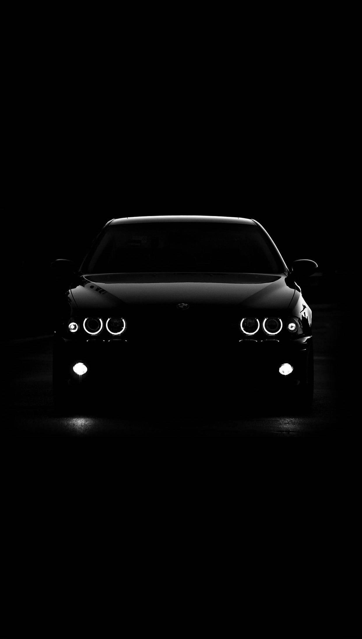 Black Bmw 桌布 壁紙 — 一輛時尚的黑色BMW汽車在漆黑一片的虛空中閃耀著車頭燈，營造出戲劇性且極簡的輪廓。