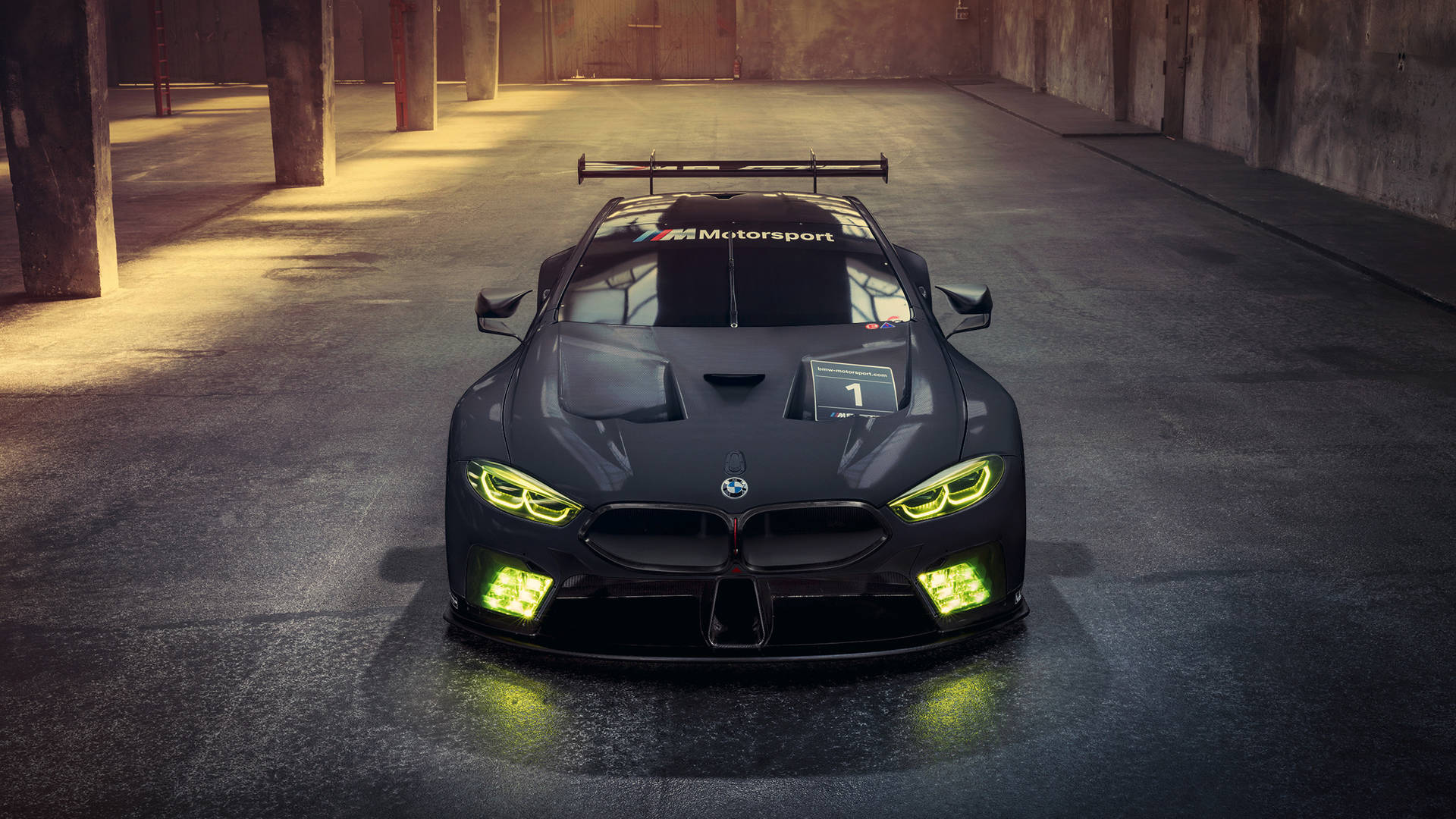 BMW 動圖 桌布 壁紙 — 一輛時尚的黑色BMW賽車，帶有發光的綠色頭燈，停放在光線昏暗的混凝土倉庫中央。
