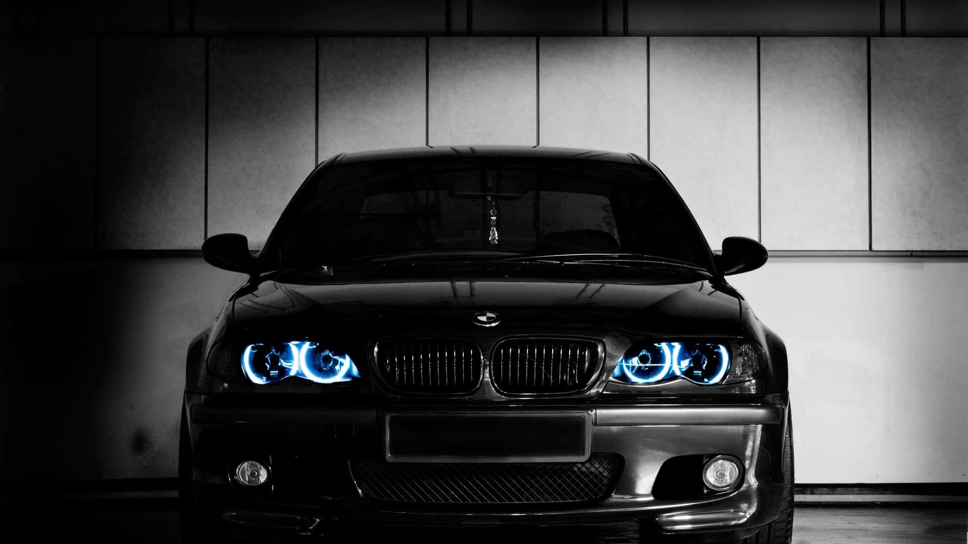 Bmw Cars 桌布 壁紙 — 一輛時尚的黑色BMW跑車，帶有發光的藍色車頭燈，在光線昏暗的車庫中向前凝視，車庫有鑲板牆。