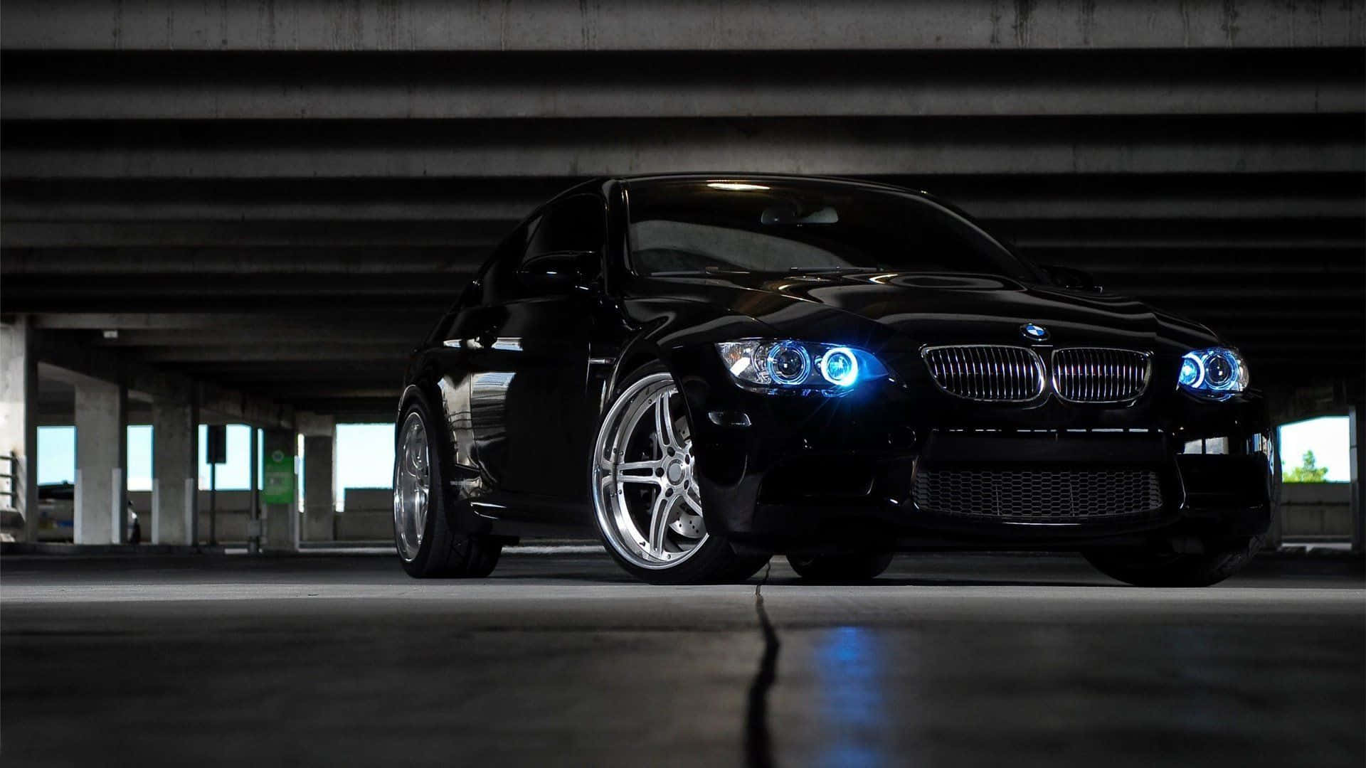 BMW 動圖 桌布 壁紙 — 一輛時尚的黑色BMW跑車，帶有發光的藍色車頭燈，夜間停在混凝土高架橋下。