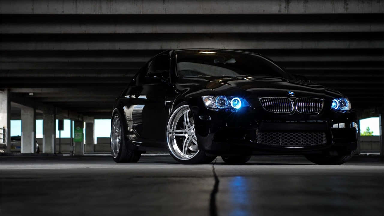 720p Bmw 桌布 壁紙 — 一輛時尚的黑色BMW跑車，帶有發光的藍色車頭燈，夜晚停在混凝土高架橋下。