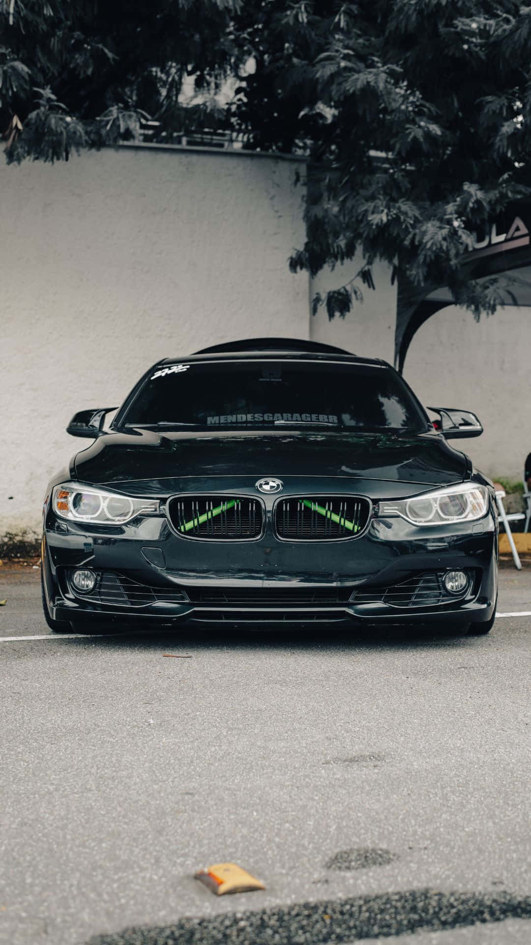 Android Bmw 桌布 壁紙 — 一輛時尚的黑色BMW跑車，帶有發光的綠色點綴，停在安靜街道上枝葉茂密的樹下。