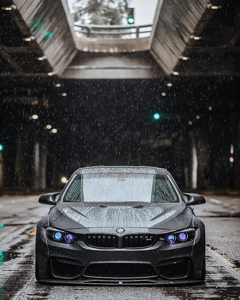 m 桌布 壁紙 — 一輛時尚的黑色BMW跑車配備發光的藍色車頭燈，在夜間行駛於被雨水浸濕的高架橋下。
