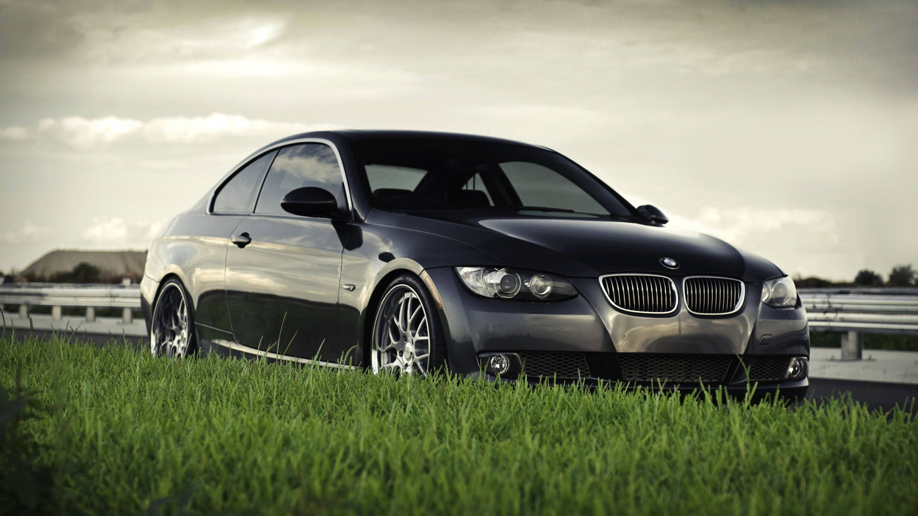 4K BMW 壁紙 桌布 壁紙 — 一輛時尚的黑色BMW雙門轎跑車停在高速公路旁的草地上，天空多雲。