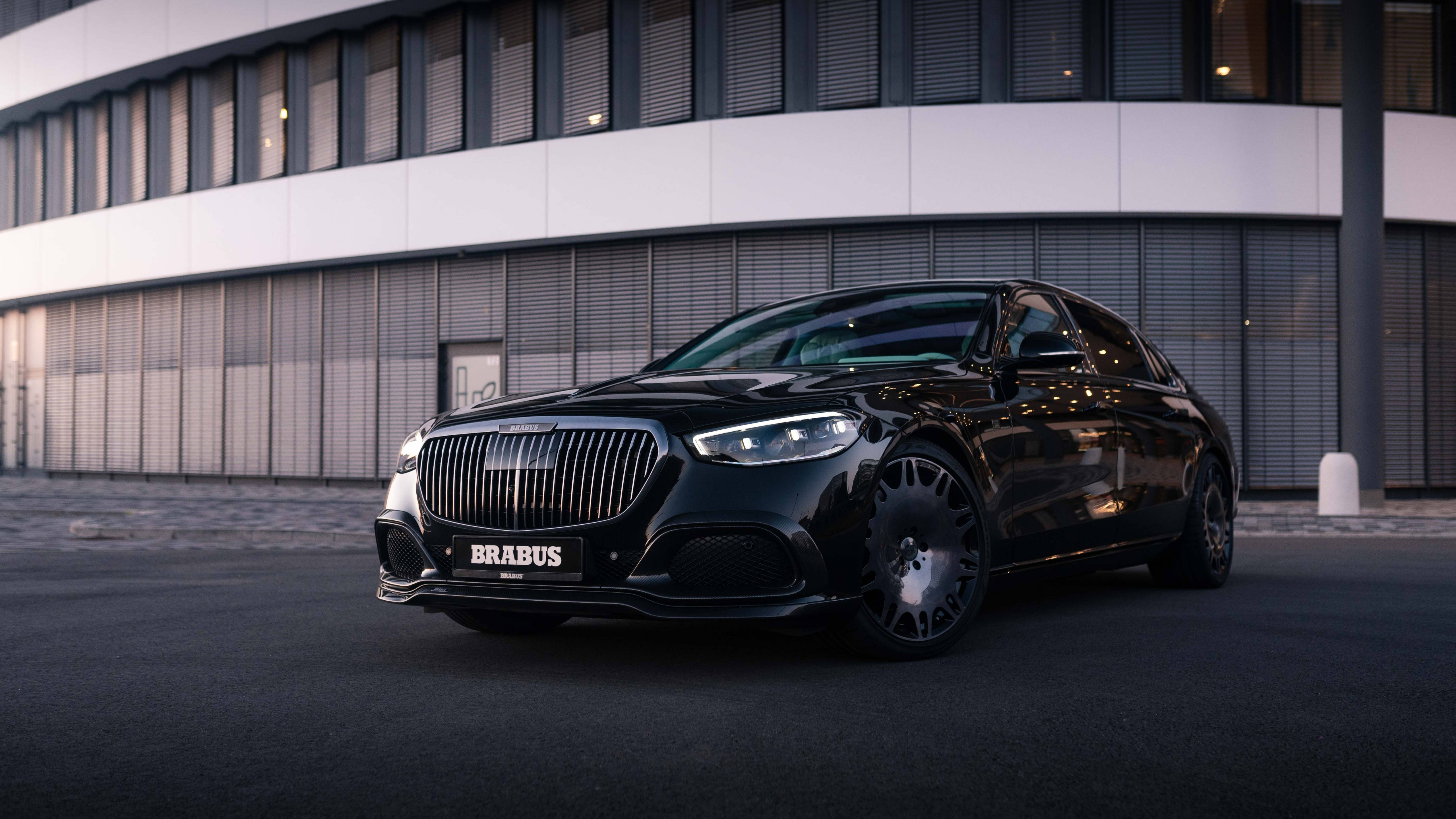 Luxury 桌布 壁紙 — 一輛時尚的黑色Brabus Mercedes轎車在暮色燈光下閃耀，停放在現代建築外牆前。