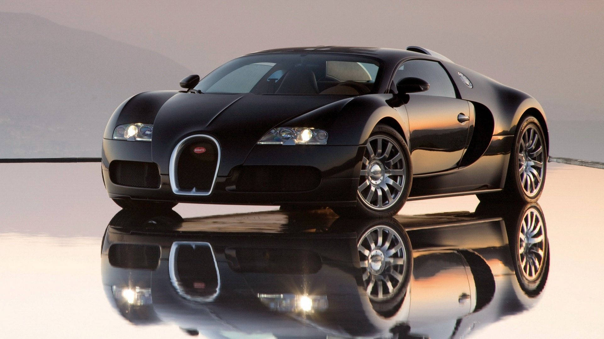 Cool Bugatti 桌布 壁紙 — 一輛時尚的黑色Bugatti超級跑車在柔和光線下閃閃發光，其完美的倒影映照在光亮的白色表面上，背景是朦朧的山巒。
