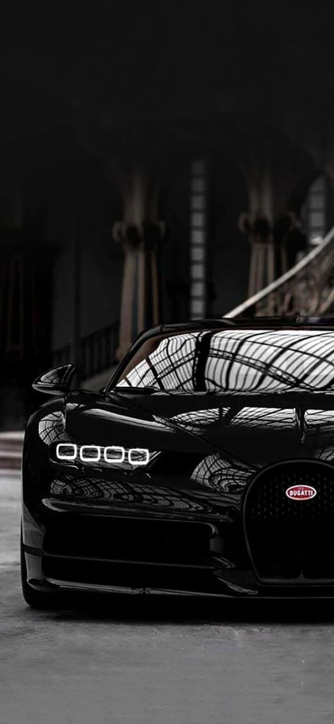 iPhone Xs Bugatti 桌布 壁紙 — 一輛時尚的黑色Bugatti超跑在宏偉陰暗的建築空間中，在戲劇性的燈光下閃閃發光。