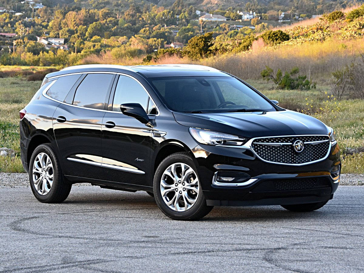 Buick 桌布 壁紙 — 一輛時尚的黑色Buick Enclave SUV停在瀝青路上，金色午後陽光下，起伏的綠色山丘和散落的房屋。