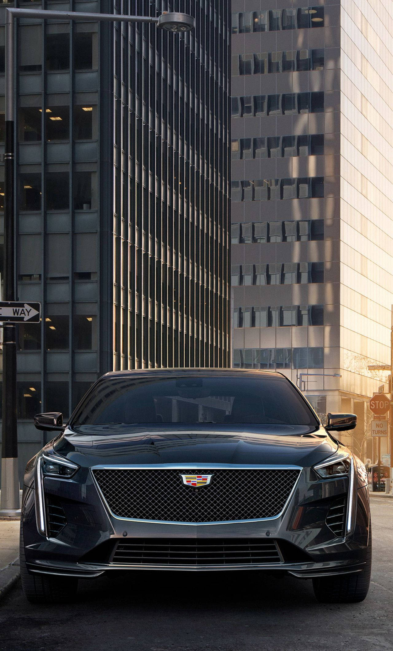 凱迪拉克 iPhone 桌布 壁紙 — 一輛時尚的黑色Cadillac CT4-V停泊在黃金時段光線沐浴下的高聳玻璃摩天大樓之間的城市街道上。