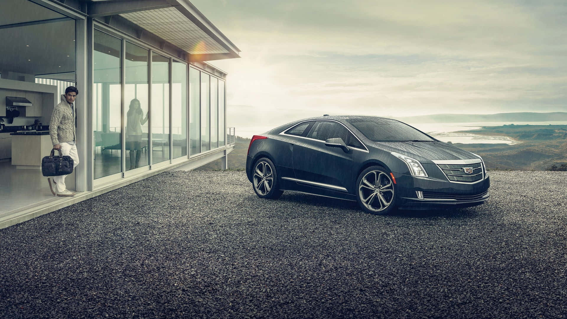 Cadillac Elr 桌布 壁紙 — 一輛時尚的黑色Cadillac ELR停泊在碎石上，旁邊是一座現代玻璃屋，一名穿著圖案外套的男子拿著公事包。