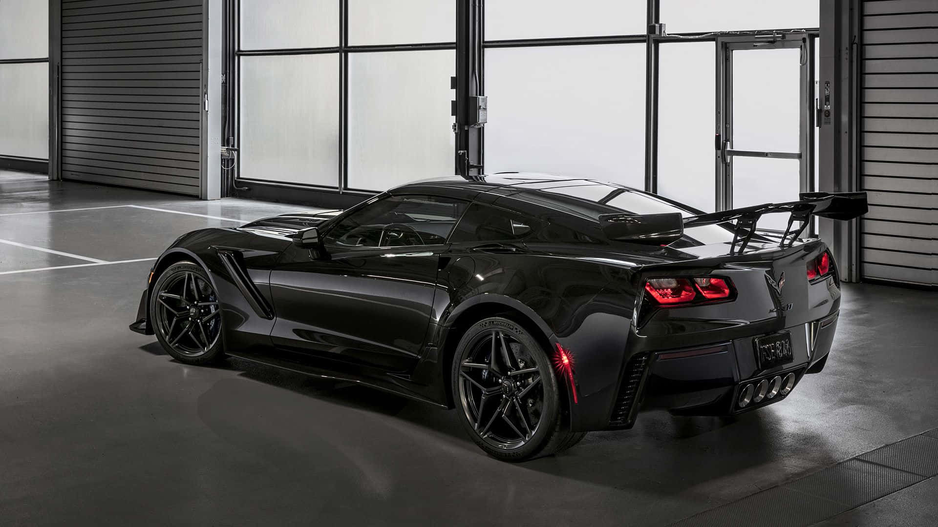 corvette 桌布 壁紙 — 一輛時尚的黑色Corvette跑車，帶有發光的紅色尾燈，停放在現代工業車庫內。