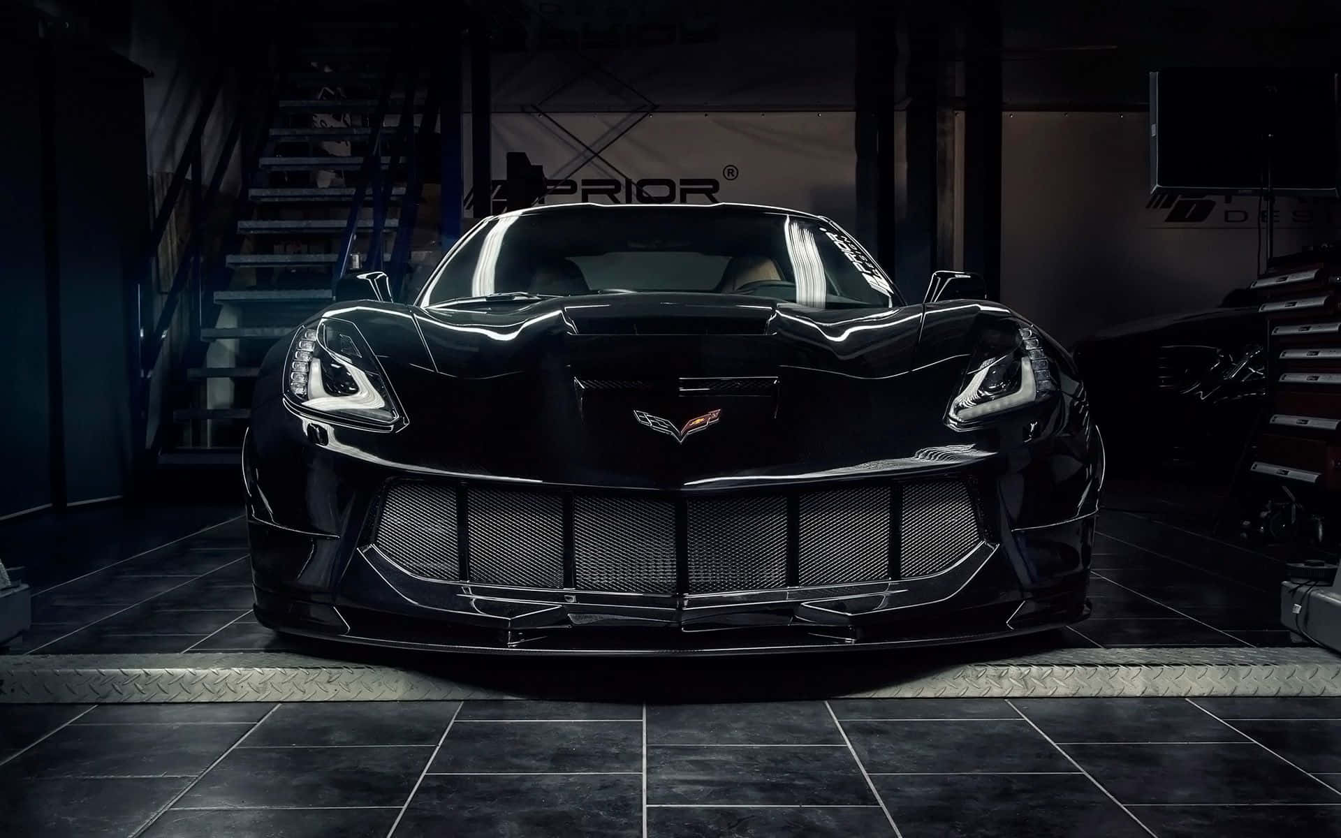 Chevrolet Corvette Stingray 桌布 壁紙 — 一輛時尚的黑色Corvette跑車在昏暗的車庫中，在戲劇性的燈光下閃閃發光，車庫鋪有瓷磚地板並配有工業設備。