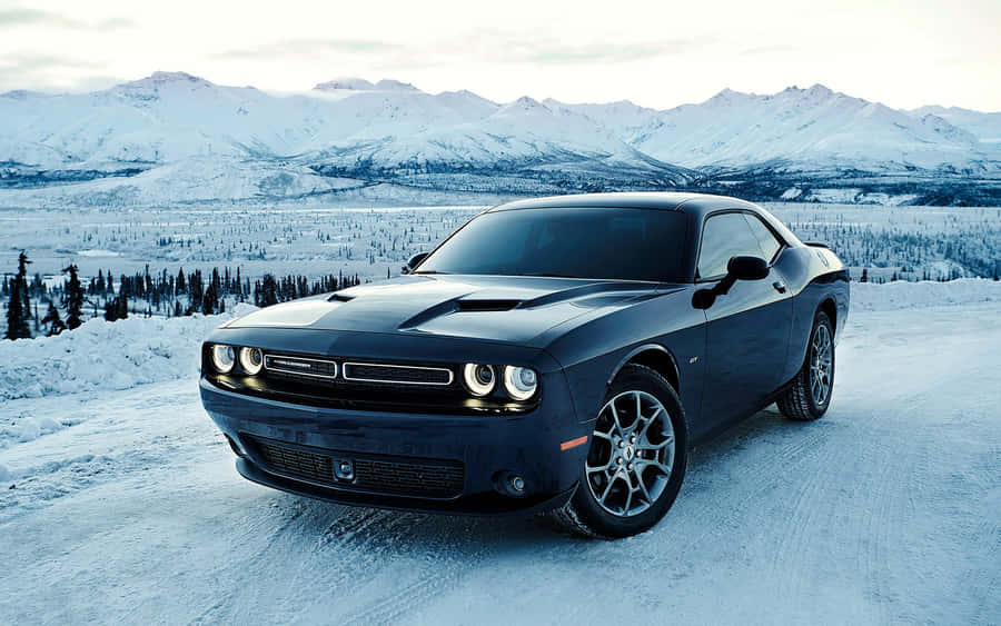 桌布 壁紙 — 一輛時尚的黑色Dodge Challenger停在雪路上，背景是白雪覆蓋的山脈，天空蒼白。