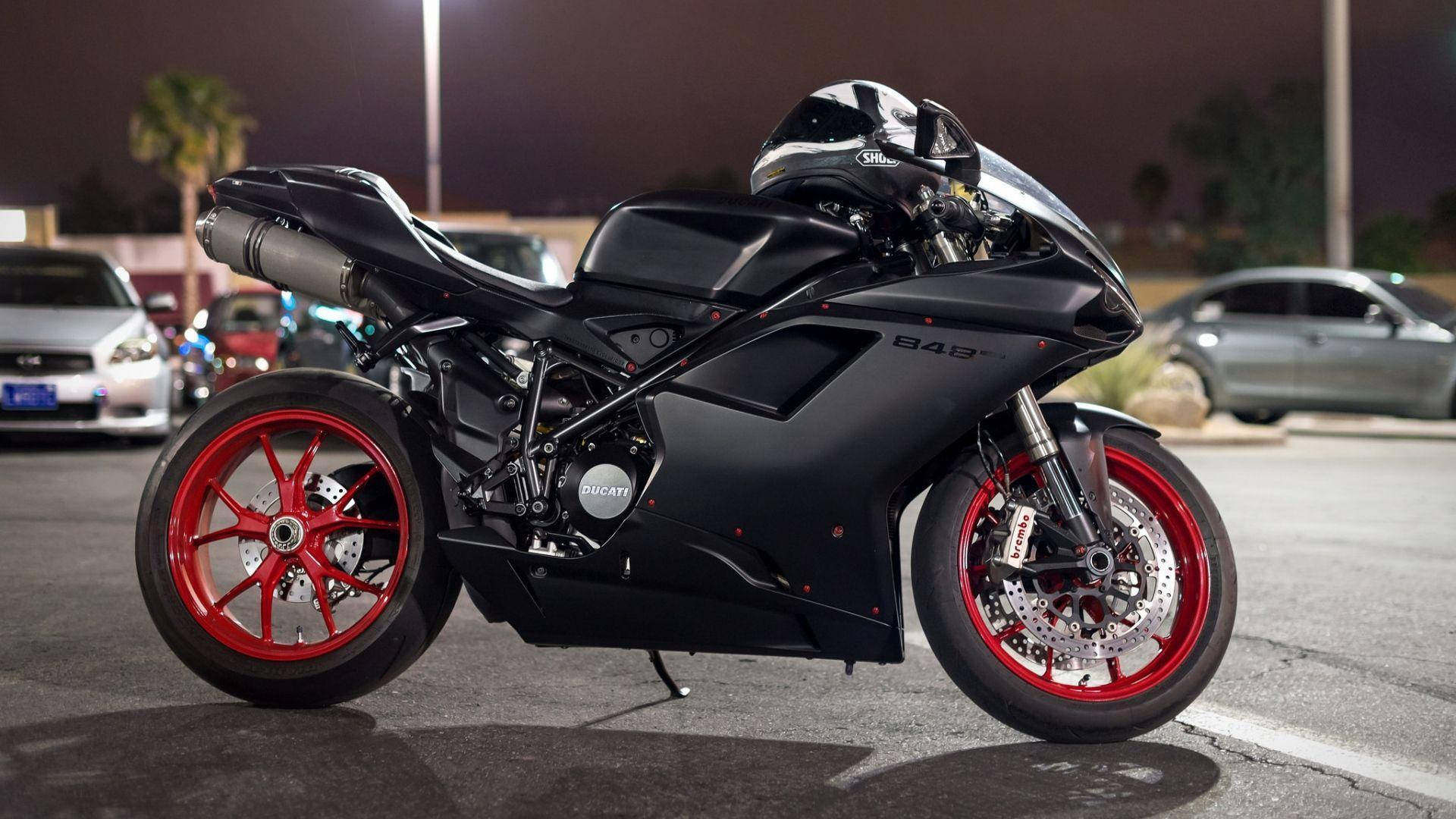機車 桌布 壁紙 — 一輛時尚的黑色Ducati摩托車，配以鮮紅色車輪，夜晚停在有燈光的停車場。