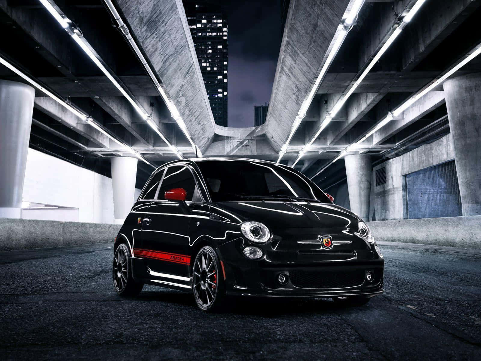 Abarth 桌布 壁紙 — 一輛時尚的黑色Fiat 500 Abarth配以紅色點綴，在夜晚現代混凝土天橋下的明亮燈光下閃閃發光。