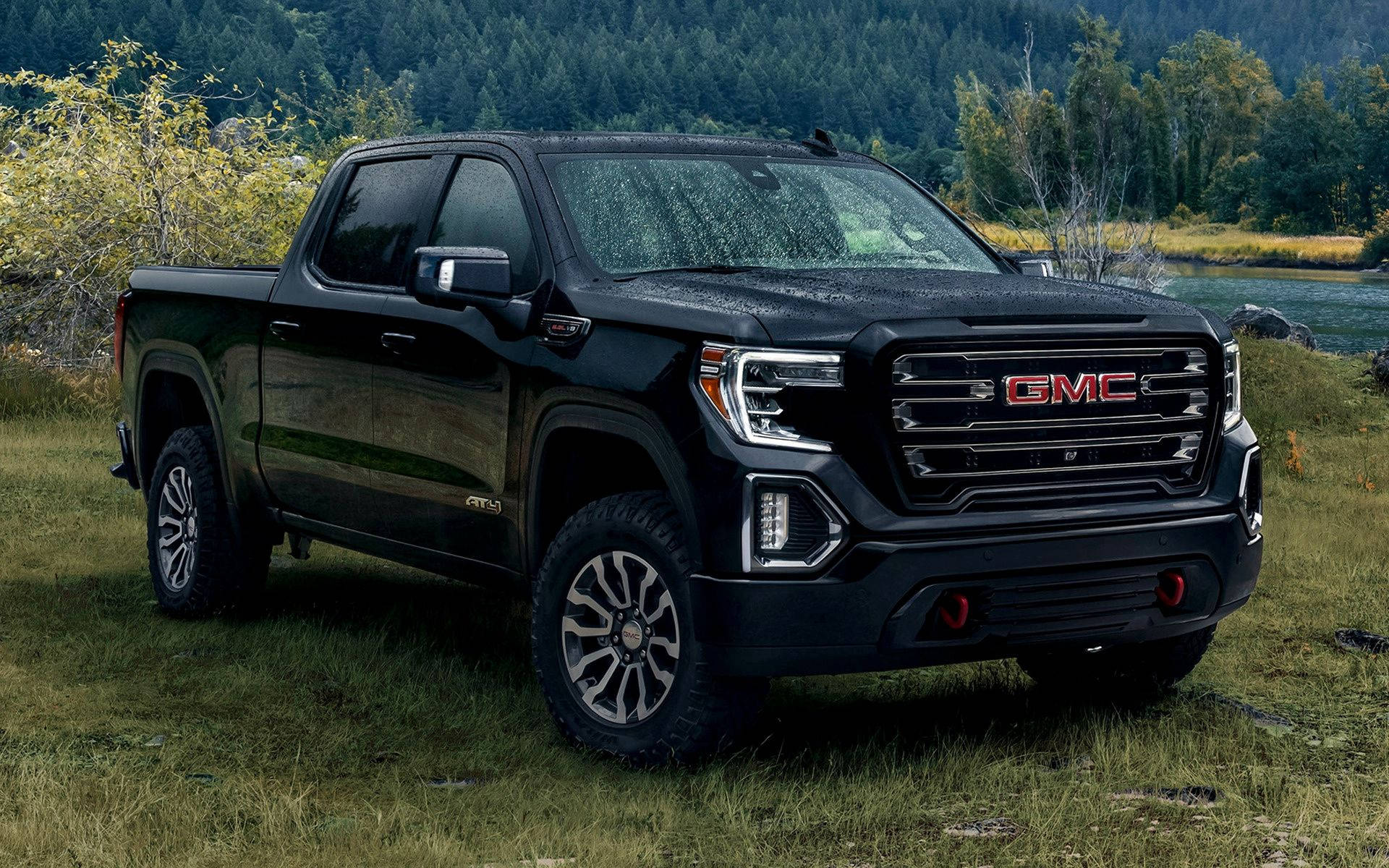Gmc 桌布 壁紙 — 一輛時尚的黑色GMC Sierra AT4 pickup truck在日光下停泊在靠近森林河岸的草地上。