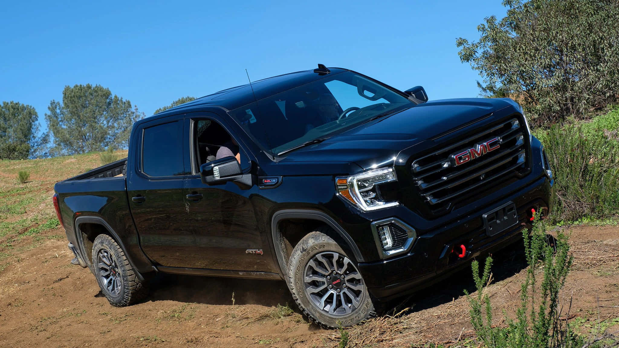 GMC 桌布 壁紙 — 一輛時尚的黑色GMC Sierra AT4 pickup truck停放在泥路上，上方是晴朗的藍天，附近有綠色灌木。