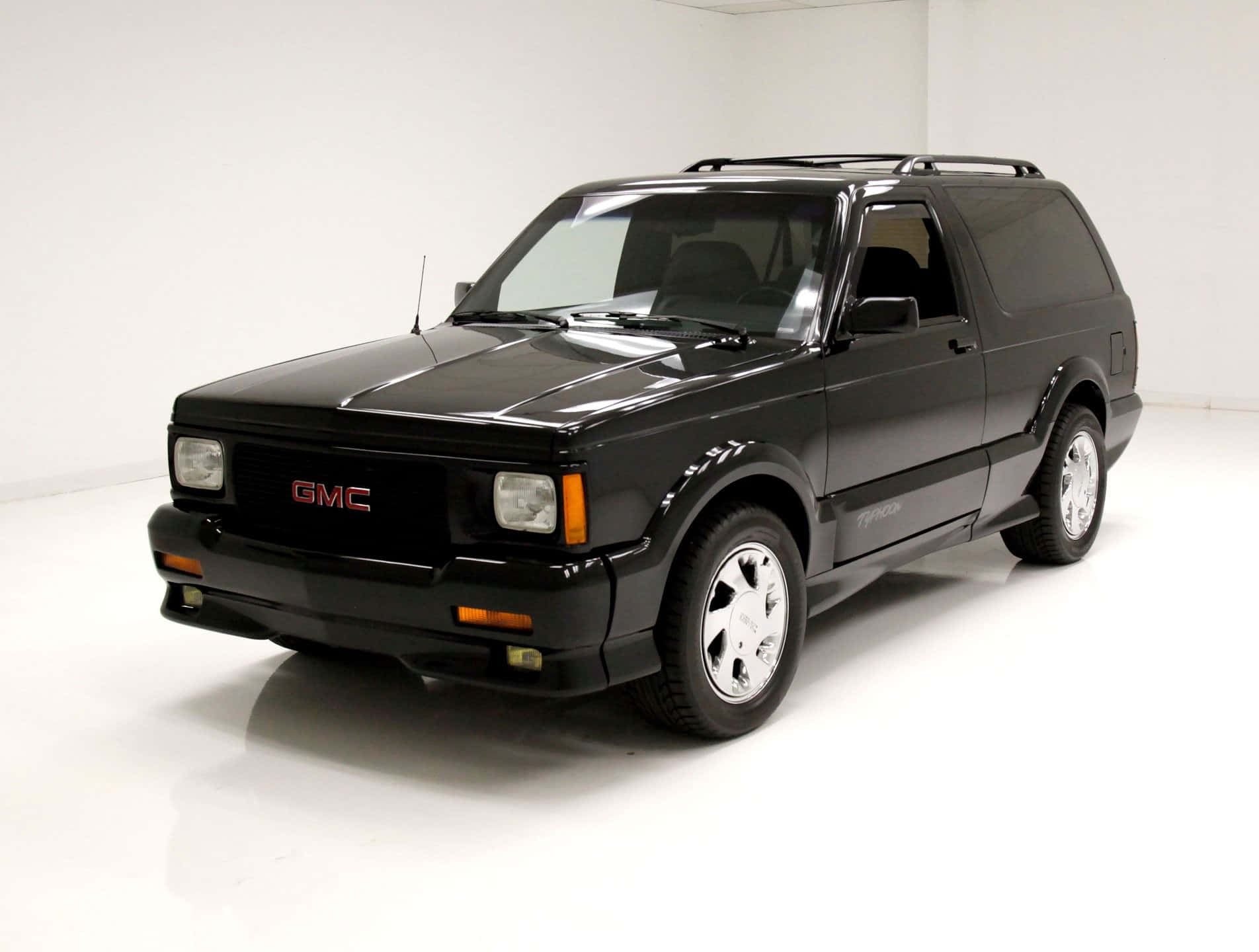 Gmc Typhoon 桌布 壁紙 — 一輛時尚的黑色GMC Typhoon SUV在明亮的攝影棚燈光下，於純白背景前閃閃發光。