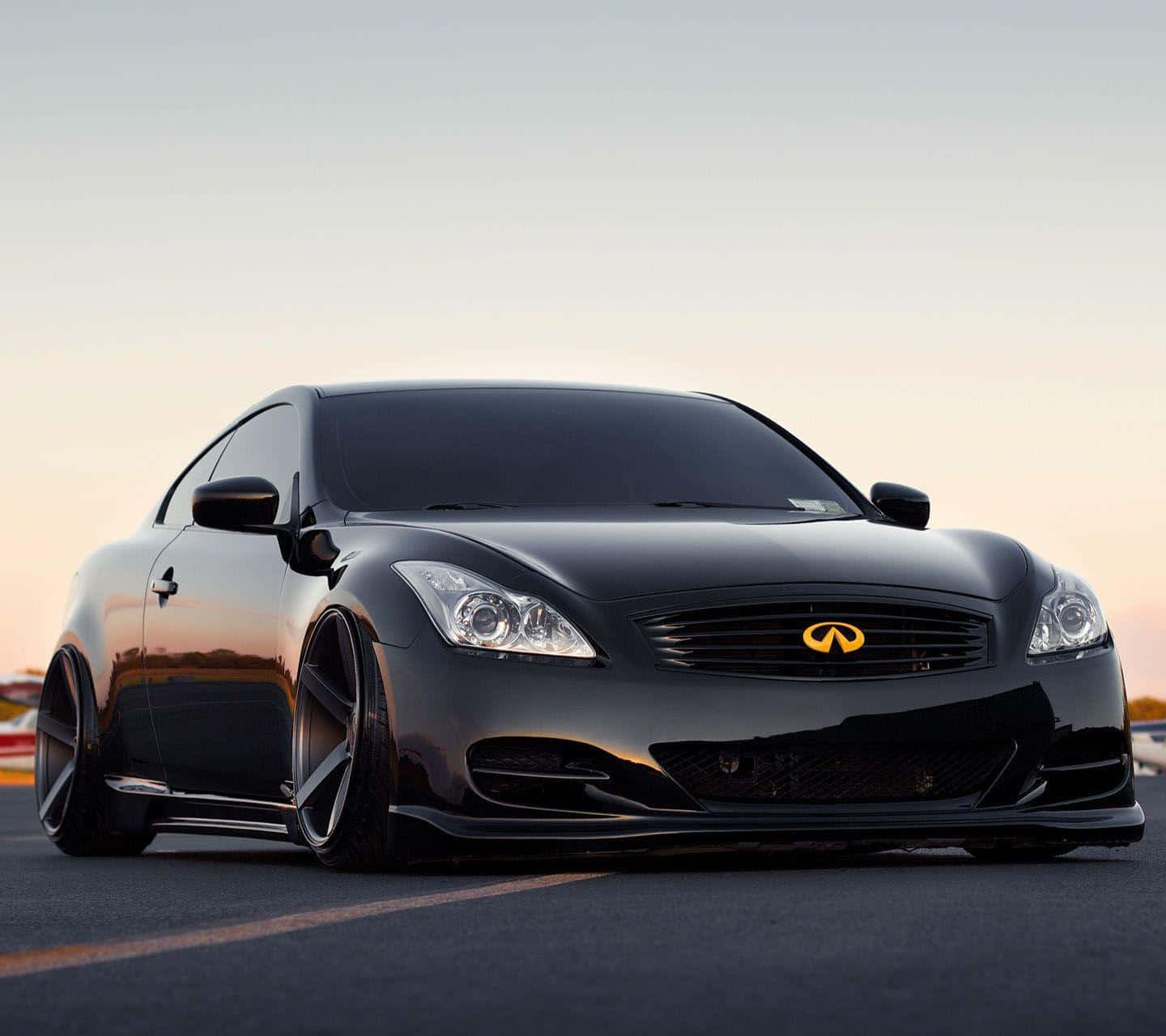 Infiniti G35 桌布 壁紙 — 一輛時尚的黑色Infiniti轎跑車配備定制輪轂，在空蕩蕩的瀝青路上閃耀著金色夕陽的光芒。
