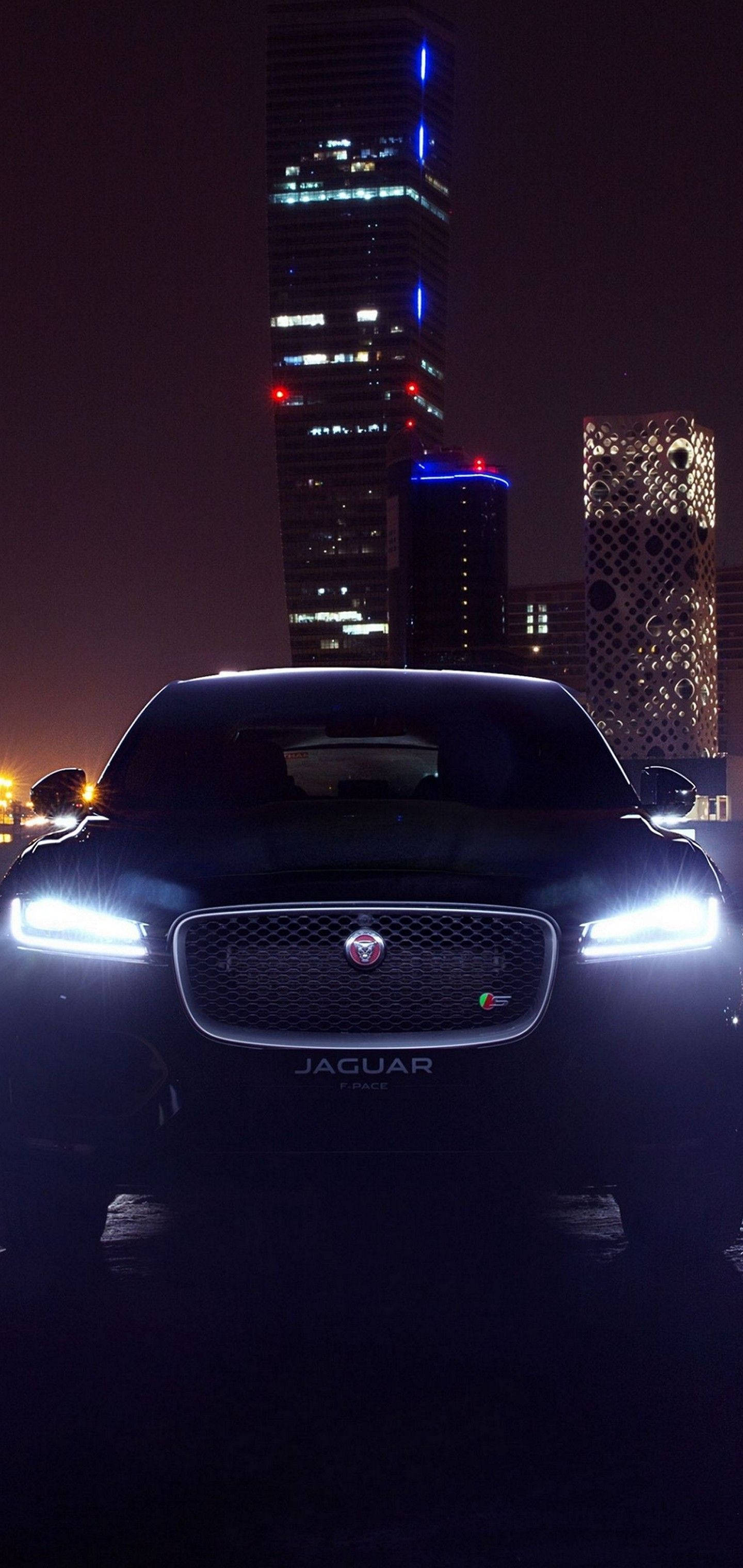 美洲豹汽車 桌布 壁紙 — 一輛時尚的黑色Jaguar F-Pace在夜間霓虹燈下，以高聳的摩天大樓為背景閃閃發光。