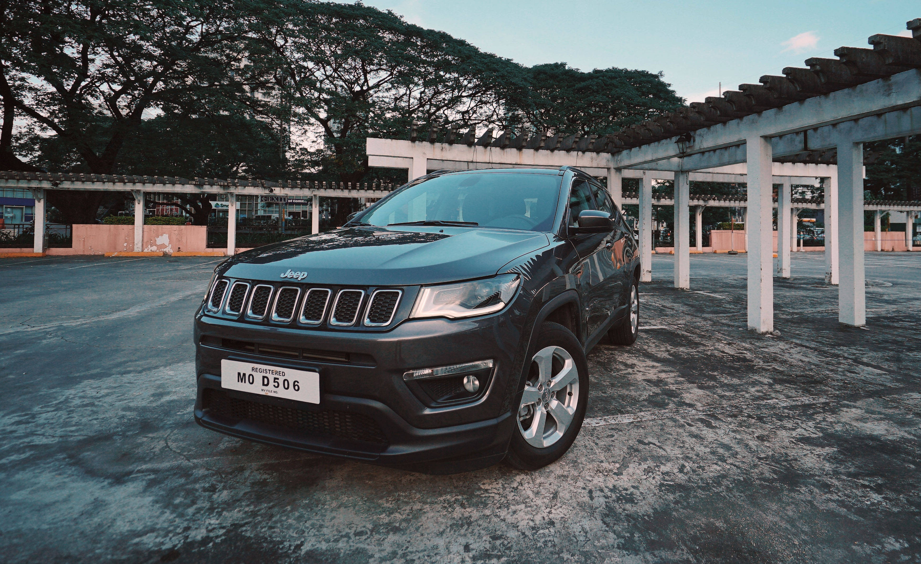 混凝土 桌布 壁紙 — 一輛時尚的黑色Jeep Compass停放在有蓋涼亭下，背景有樹木和晴朗的天空。