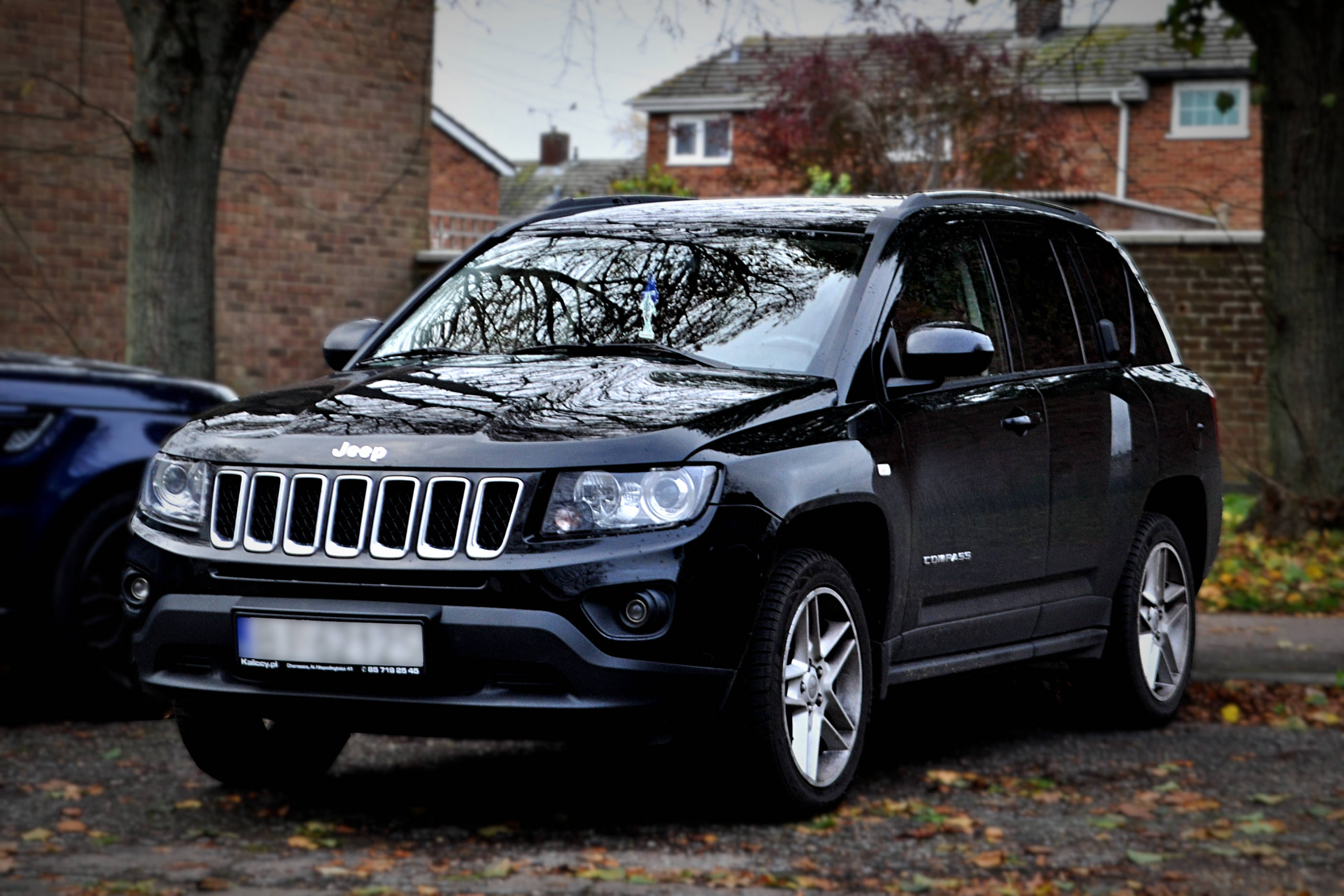 Leaves 桌布 壁紙 — 一輛時尚的黑色Jeep Compass SUV停泊在鋪滿落葉的車道上，背景是磚屋和光禿禿的樹木。