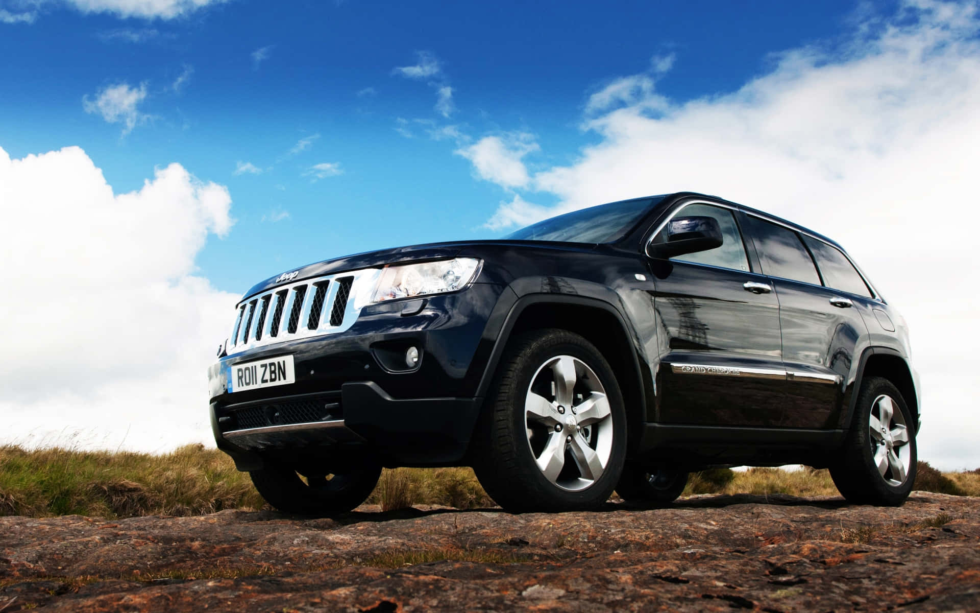 Ssangyong 桌布 壁紙 — 一輛時尚的黑色Jeep Grand Cherokee在藍天白雲下矗立在堅固的岩石上。