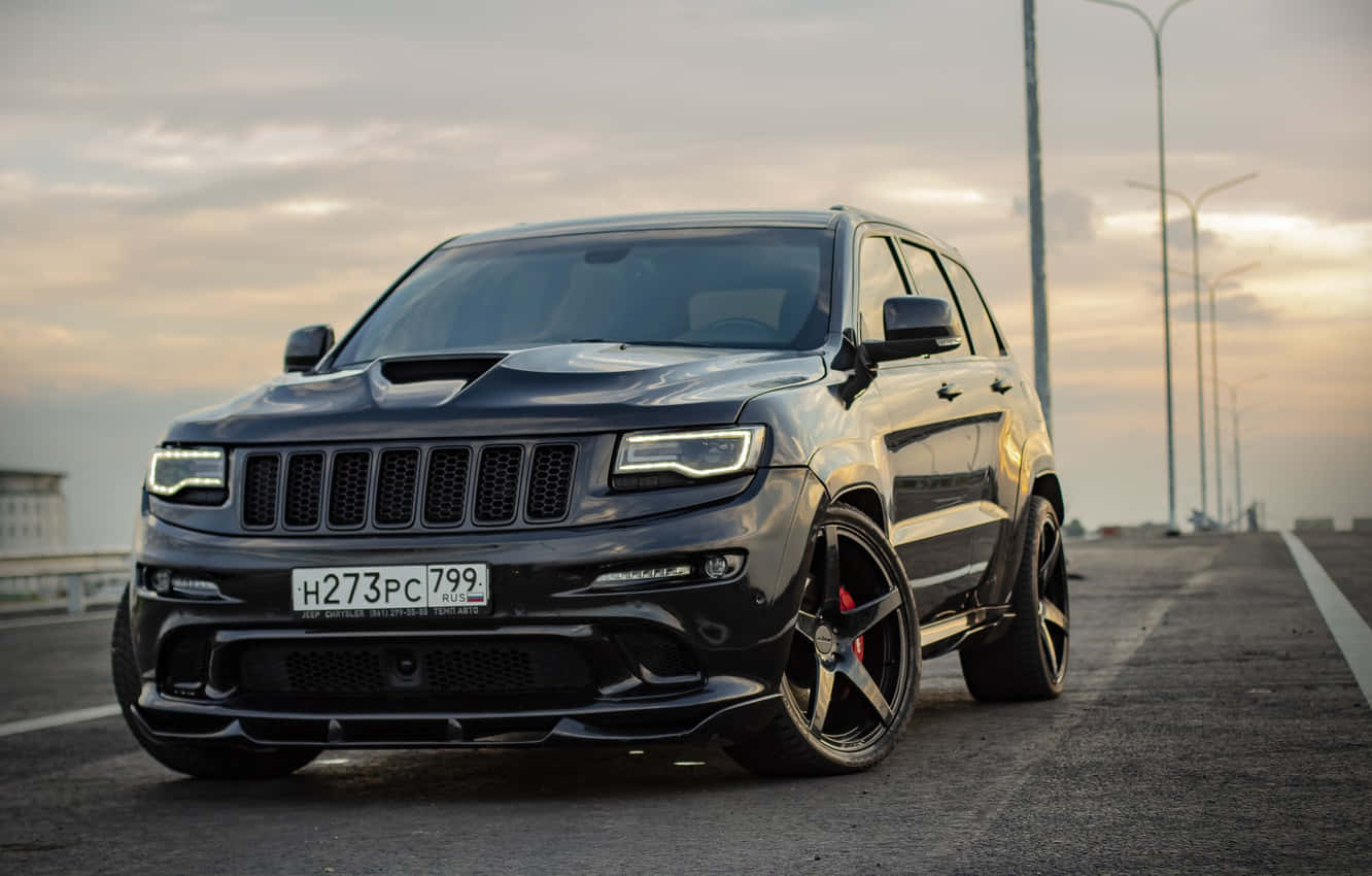 Jeep Trackhawk 桌布 壁紙 — 一輛時尚的黑色Jeep Grand Cherokee SRT停在日落時分的高速公路上，車頭燈閃爍，紅色制動卡鉗。