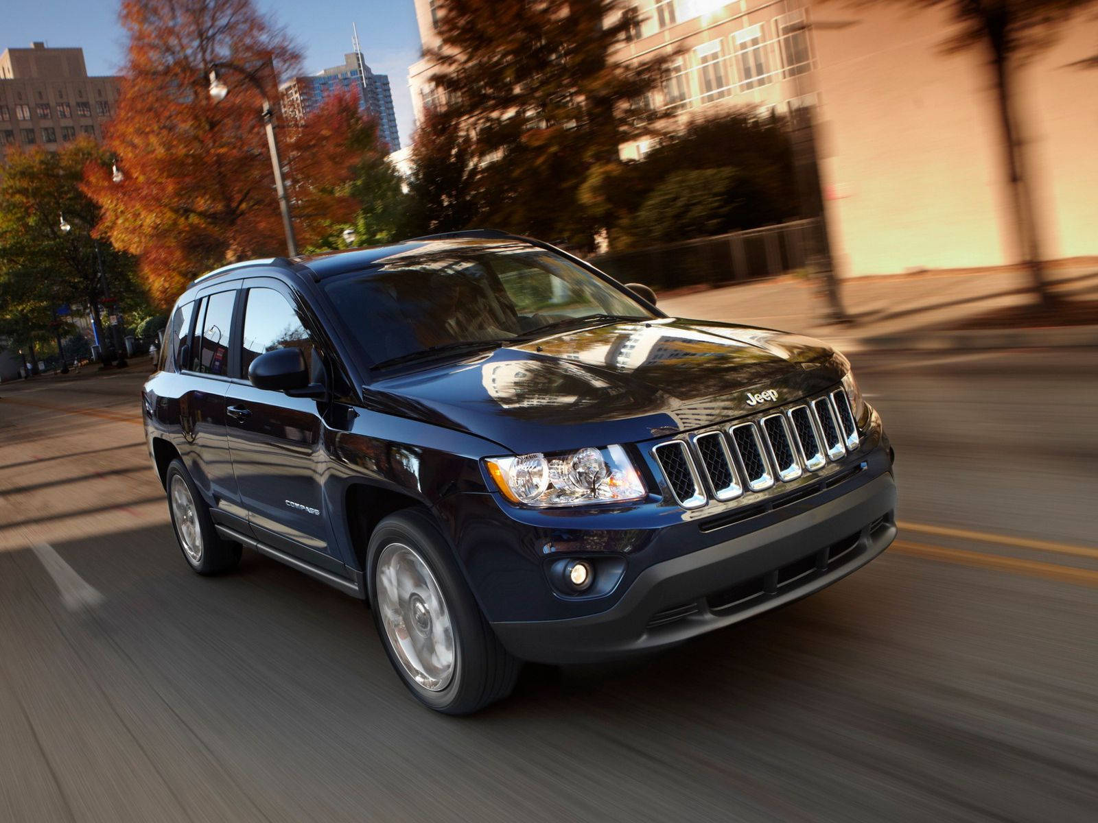 Road 桌布 壁紙 — 一輛時尚的黑色Jeep Patriot在金色陽光下，沿著兩旁種滿秋樹的城市街道飛馳。