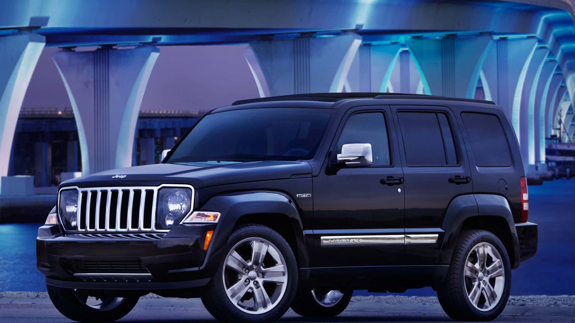 Jeep Liberty 桌布 壁紙 — 一輛時尚的黑色Jeep Patriot SUV在黃昏時停放在現代藍色照明橋下。