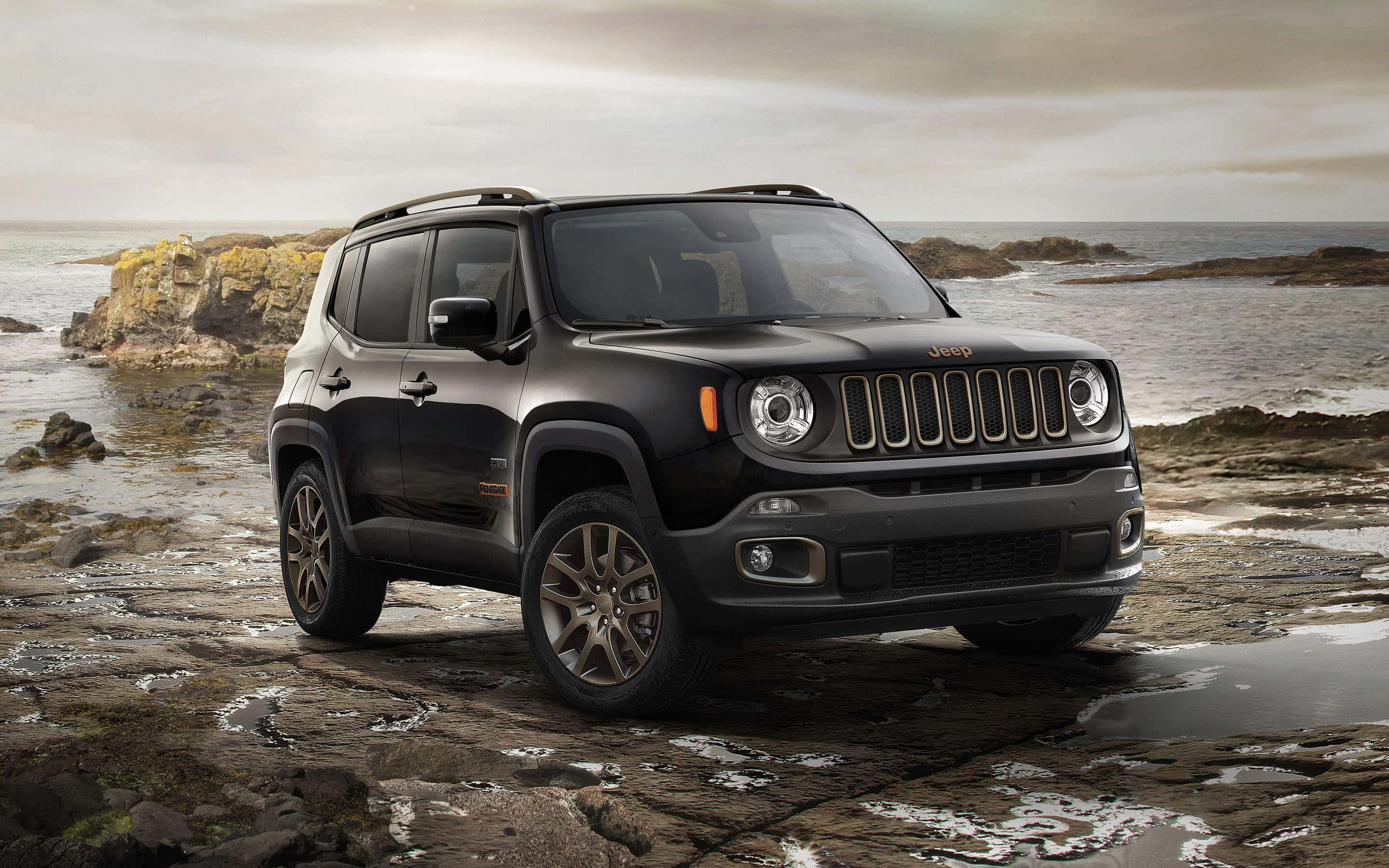 Jeep Renegade 桌布 壁紙 — 一輛時尚的黑色Jeep Renegade停在濕漉漉的海岸岩石上，背後是洶湧的海浪和陰天。