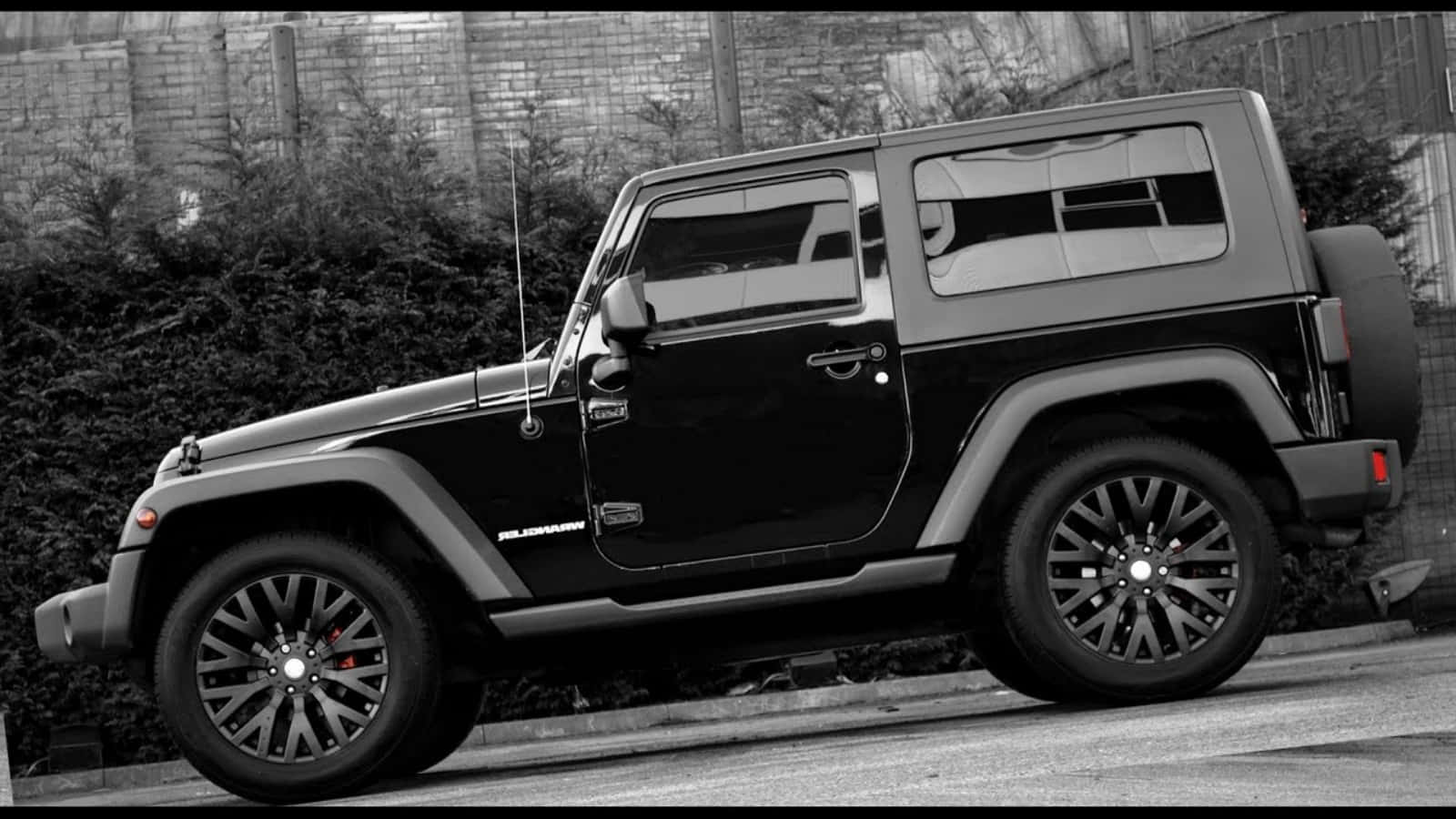 黑色吉普車 桌布 壁紙 — 一輛時尚的黑色Jeep Wrangler停在街上，背景有磚牆和灌木叢。