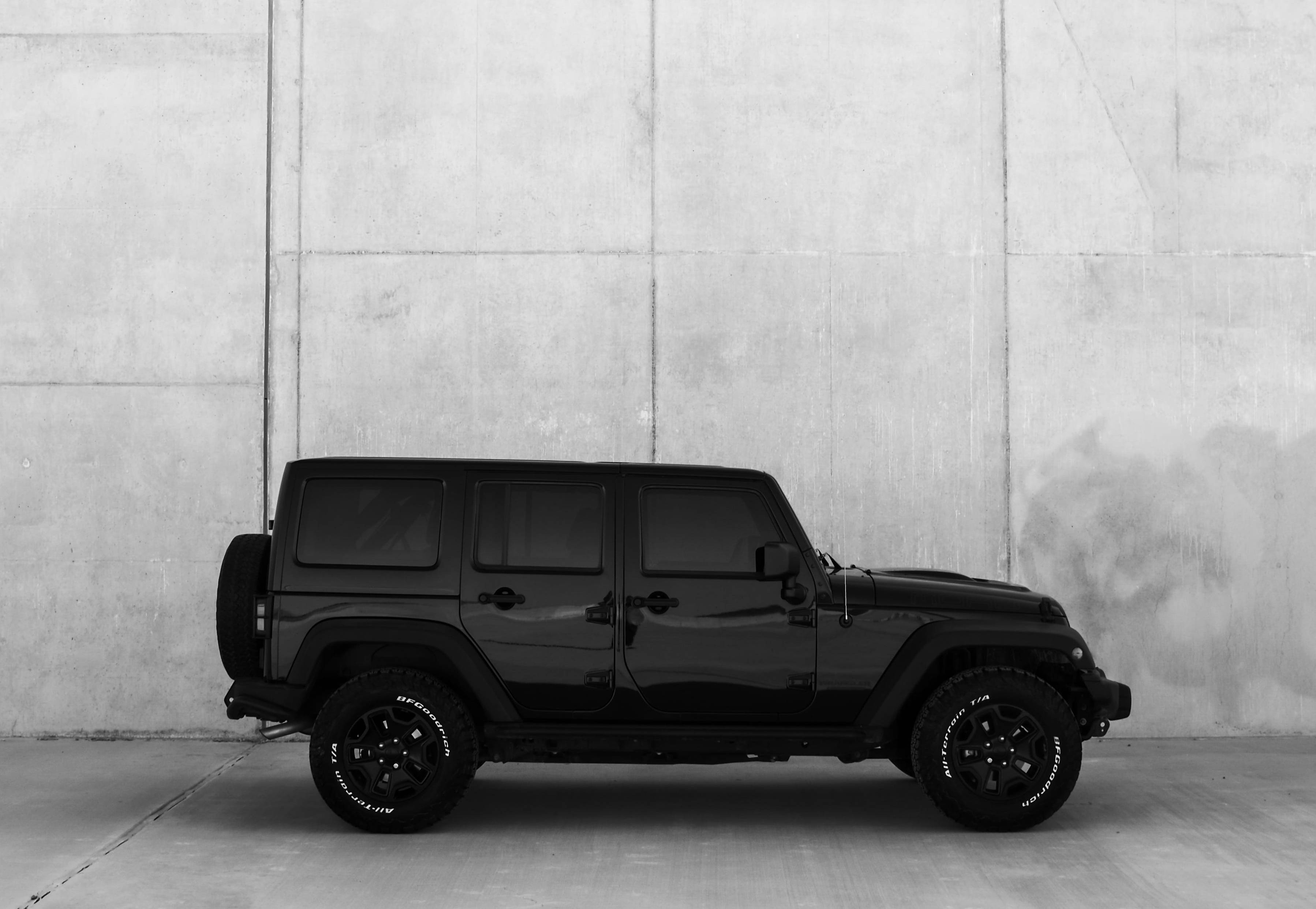黑色吉普車 桌布 壁紙 — 一輛時尚的黑色Jeep Wrangler以側面輪廓停在有紋理的混凝土牆前，呈現單色調。
