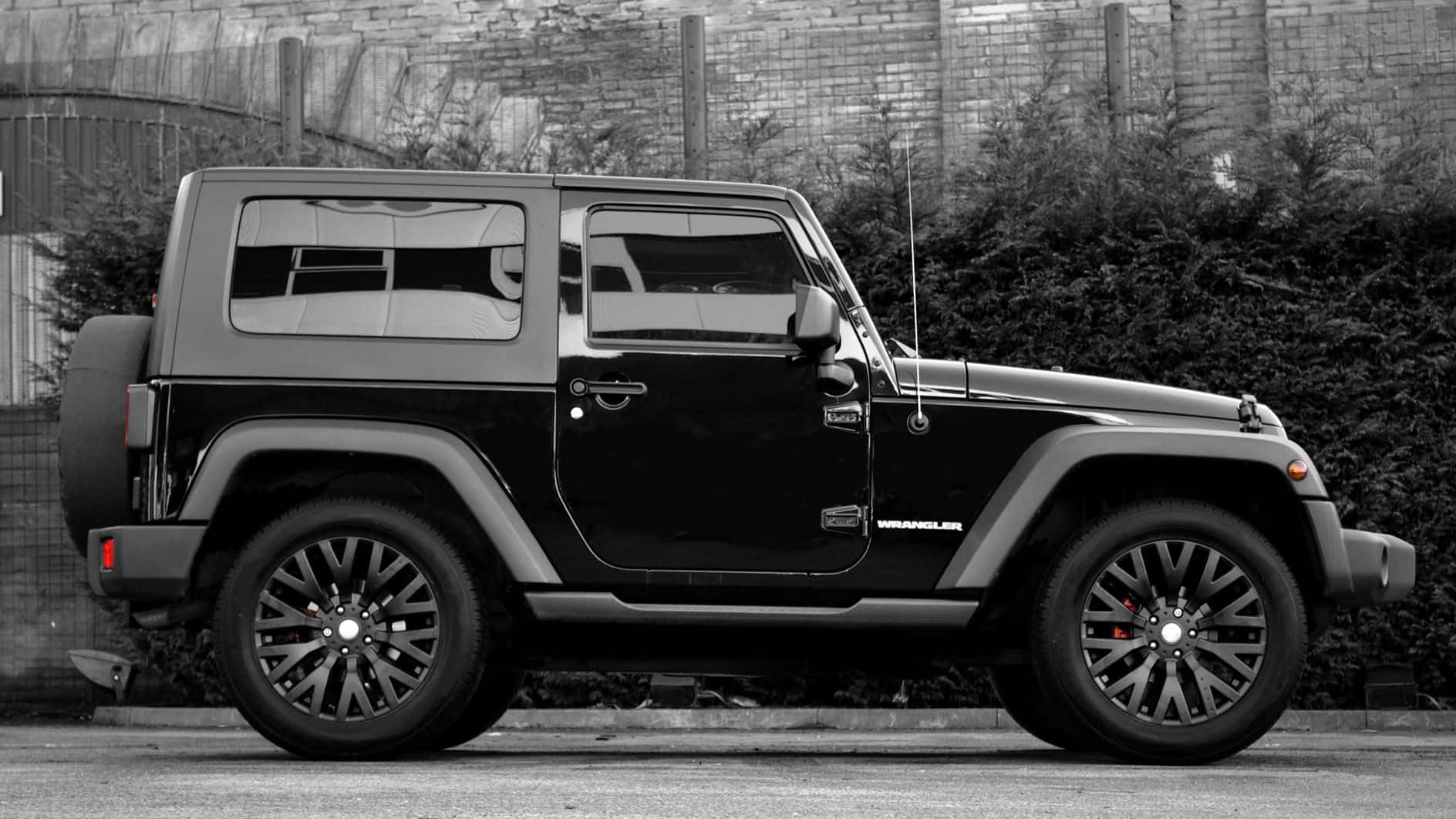 黑色吉普車 桌布 壁紙 — 一輛時尚的黑色Jeep Wrangler停在人行道上，背景有磚牆和樹籬。